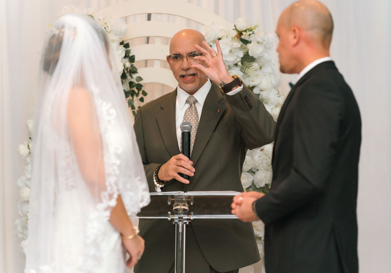 Indoor wedding ceremony with white backdrop and officiants at the altar.