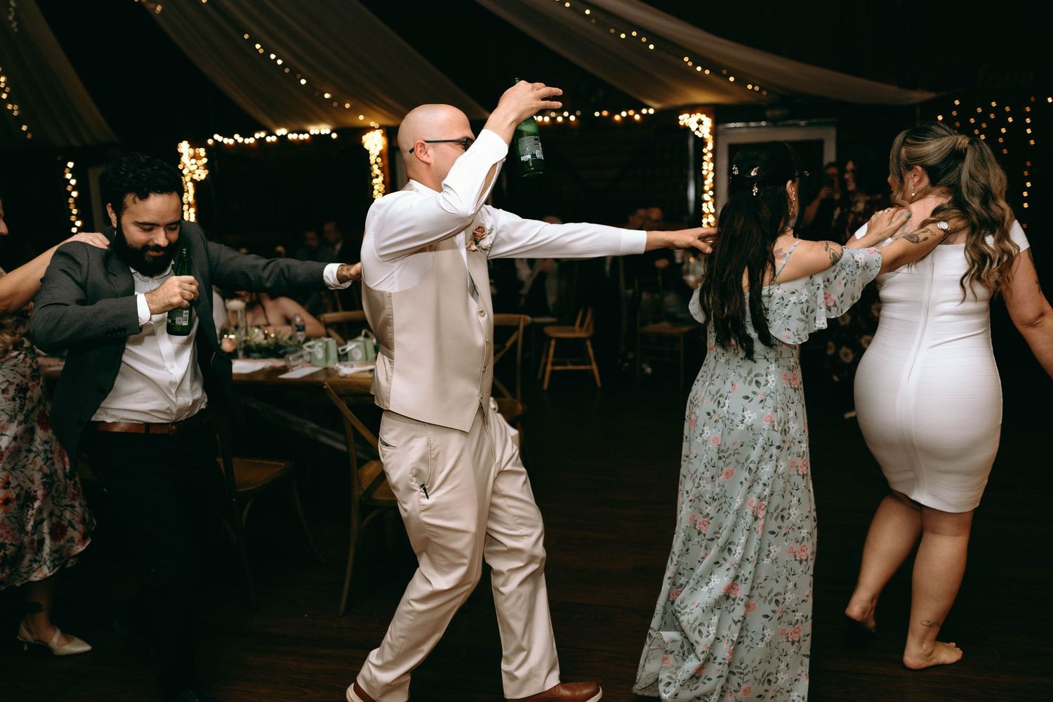 Wedding guests dance together in a line on the dance floor at an evening reception celebration.