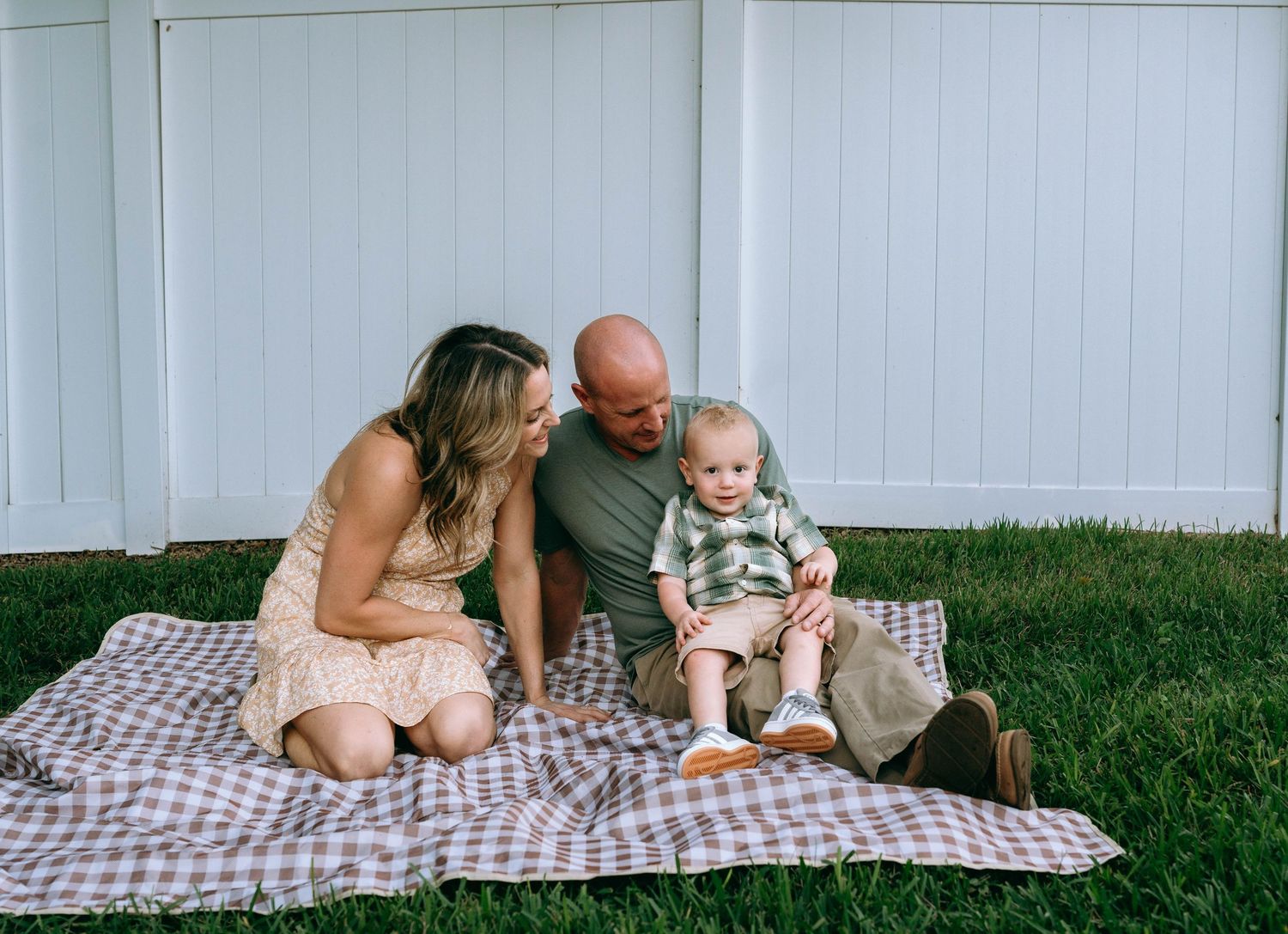 Family spending quality time together outdoors on checkered blanket.