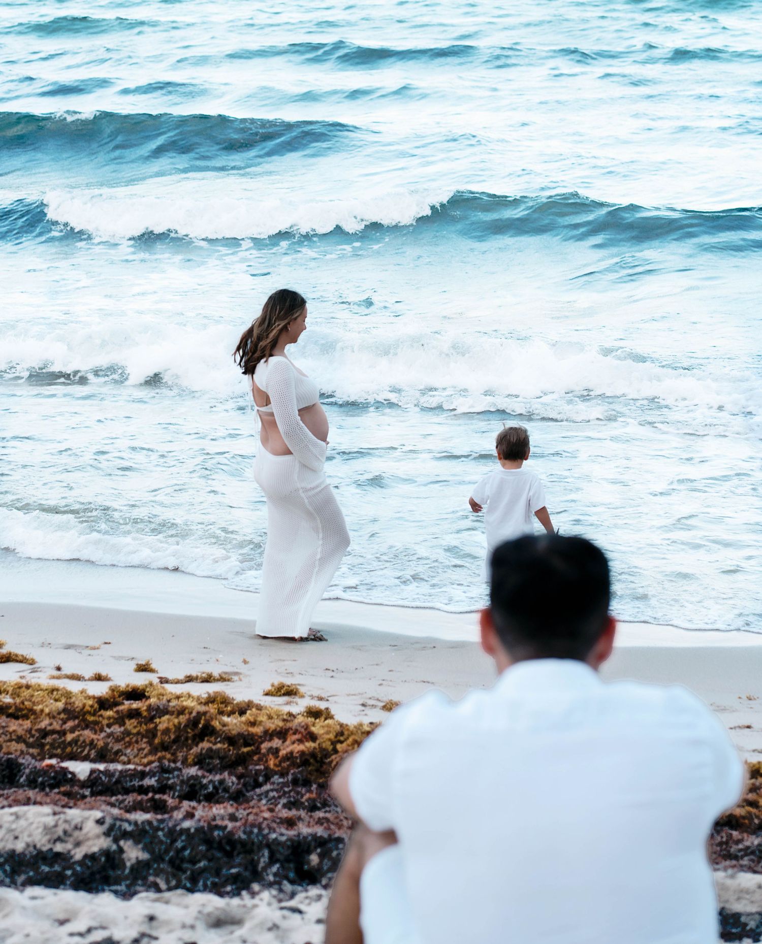 Family walking along beach shoreline in white clothing.