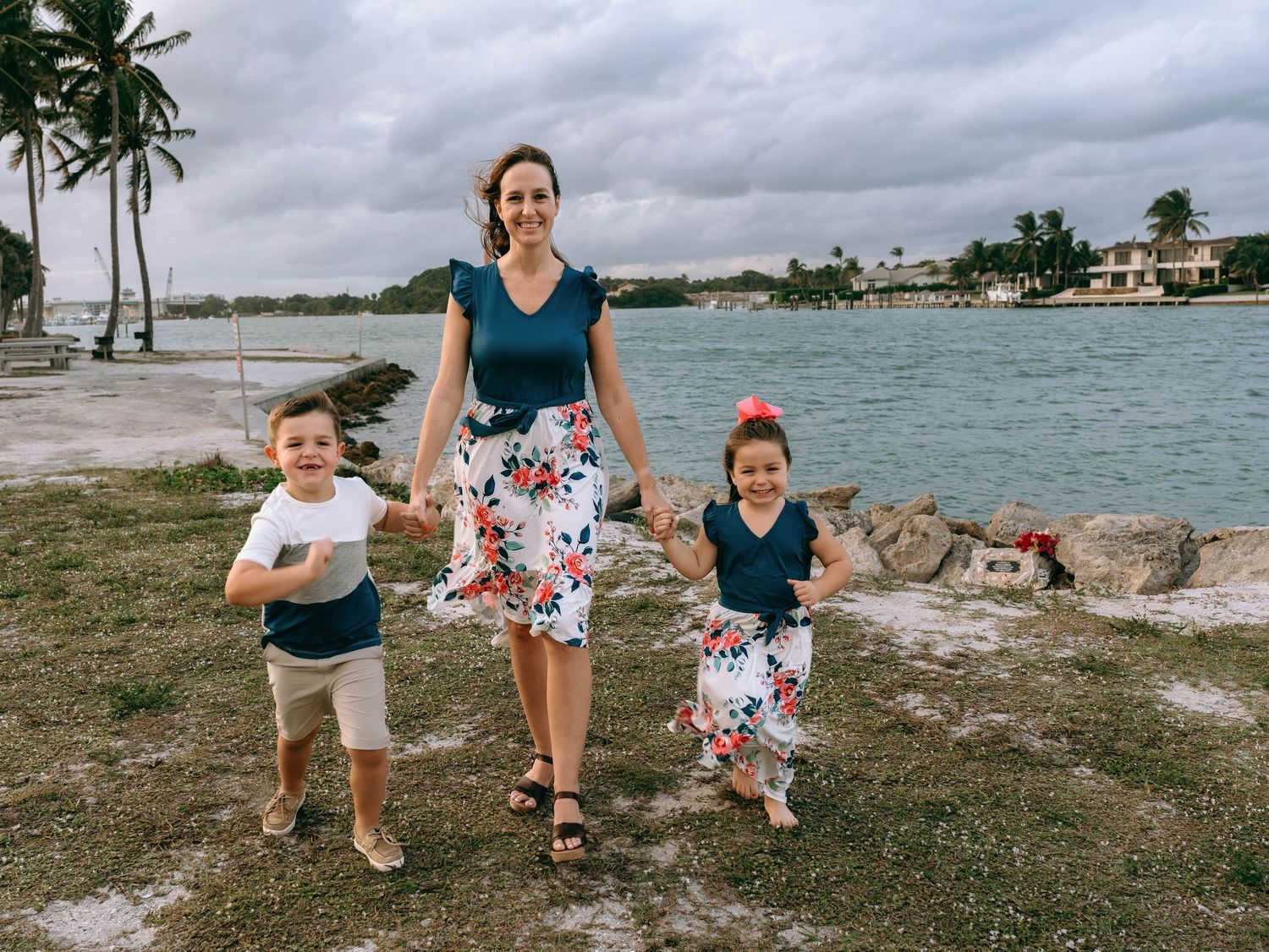 Family walking along a scenic beachfront path with palm trees and water views.