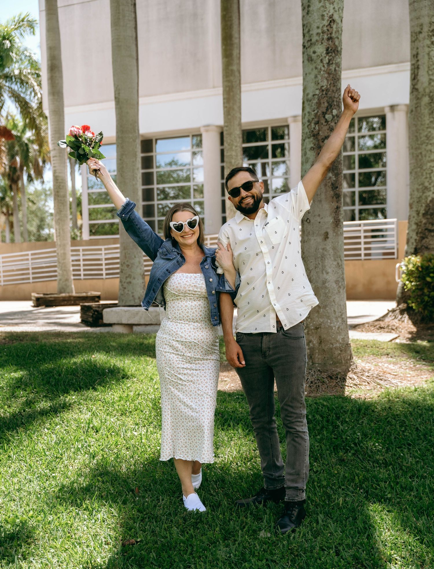 Couple dancing and celebrating outdoors near white pillars and palm trees.