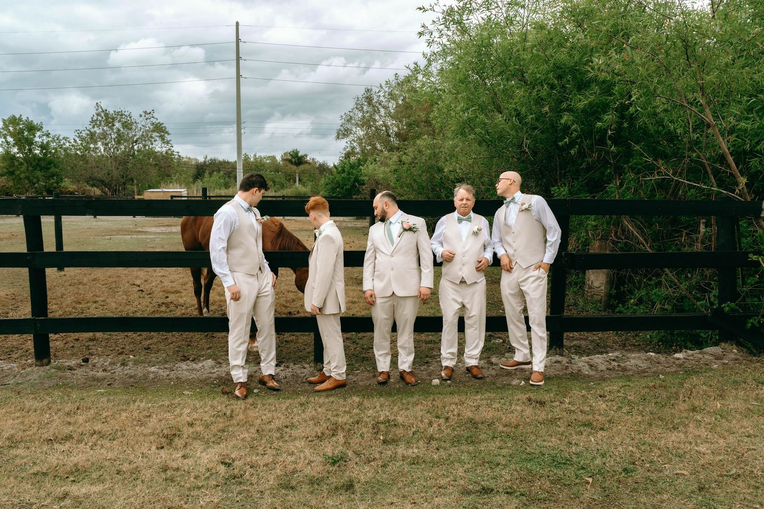 A group in white attire walks through a natural outdoor setting with trees and grass in the background.