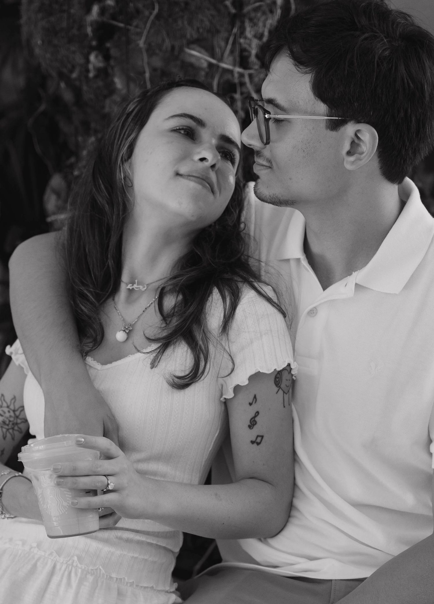 Black and white photo of a young couple sharing a tender moment, woman in white dress holding a drink. Engagement photos on Worth Avenue