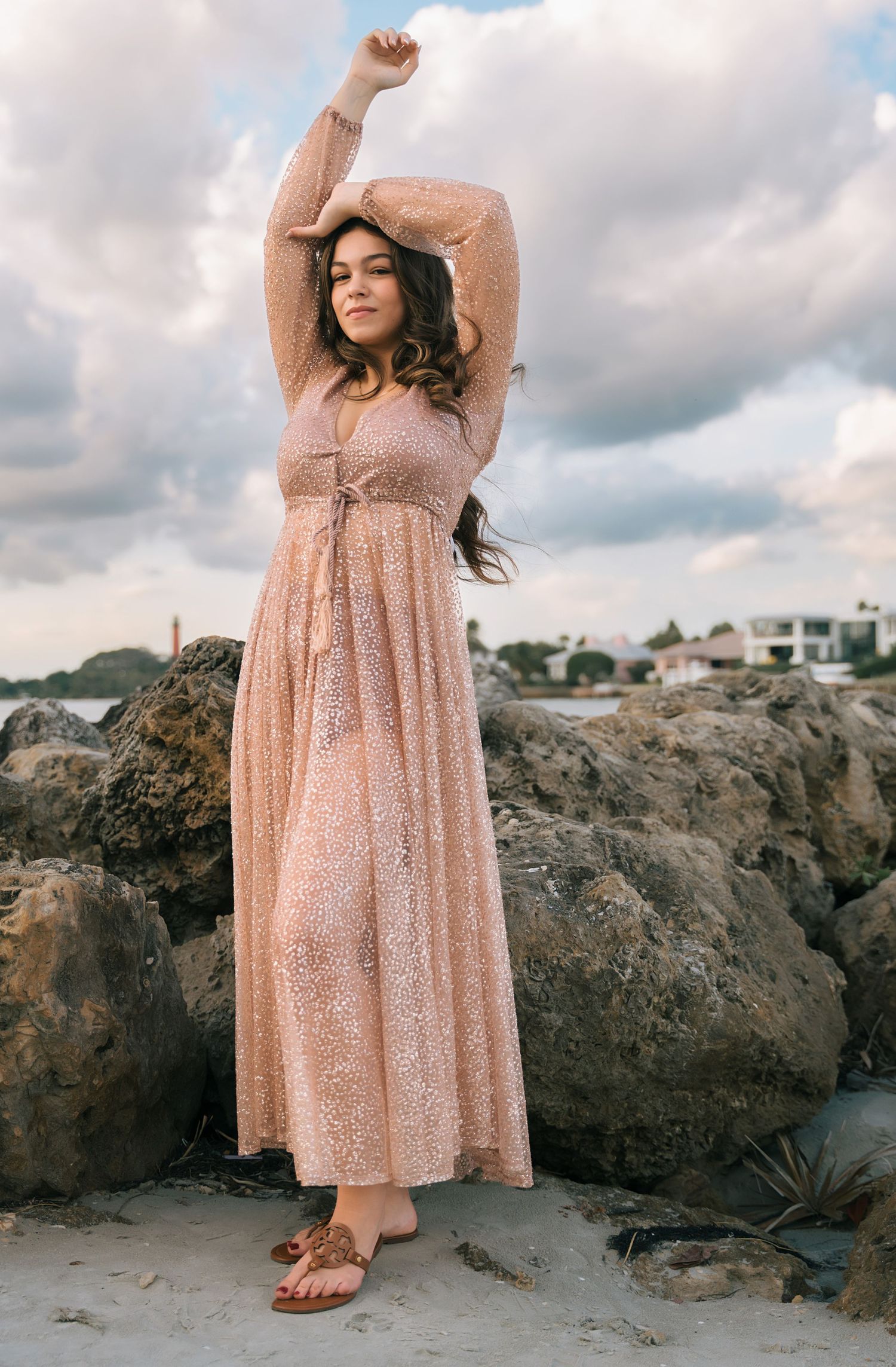 Romantic beach photoshoot with flowing peach dress against rocky coastal backdrop.
