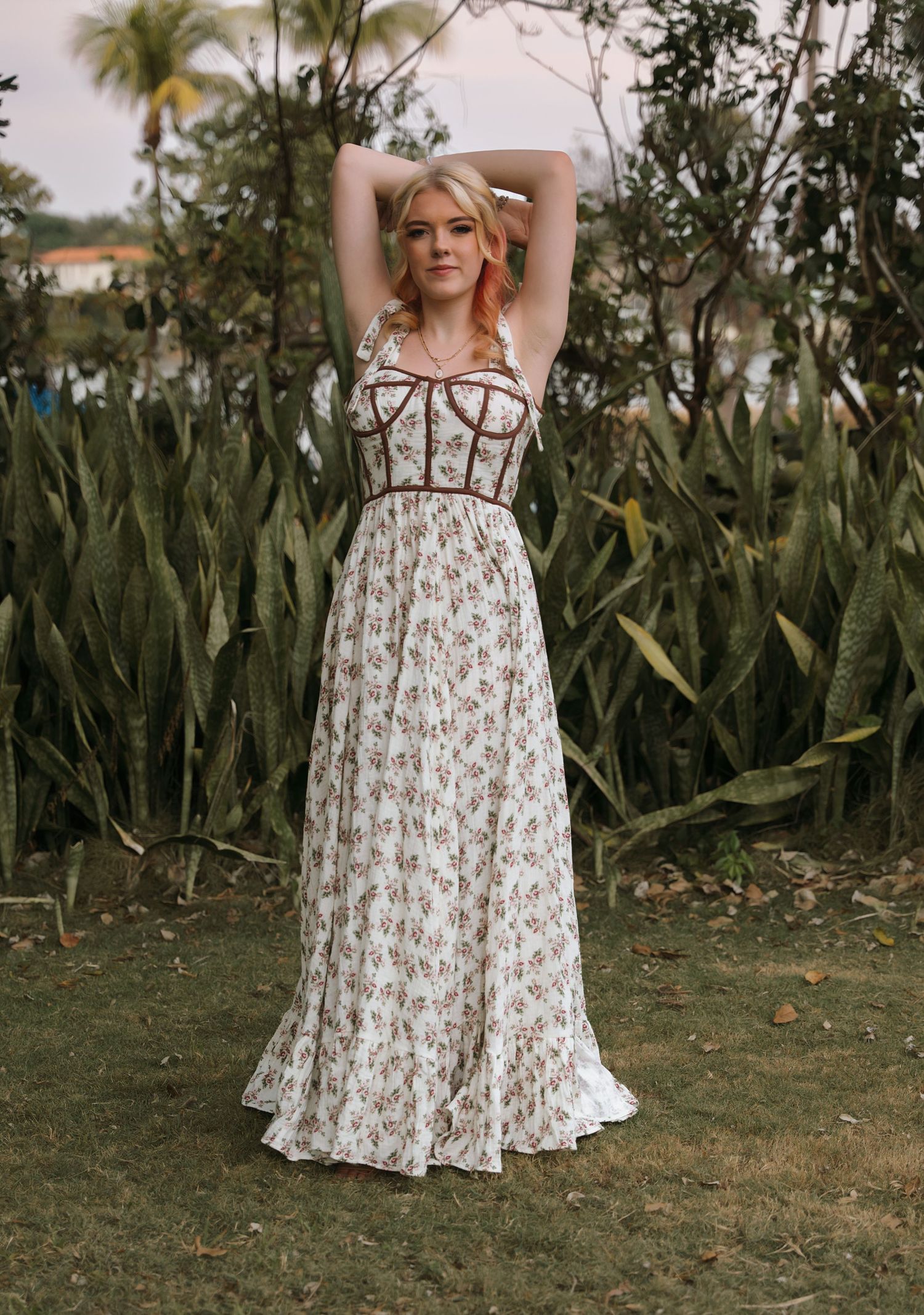 A white floral maxi dress with corset bodice detail photographed against lush tropical foliage.