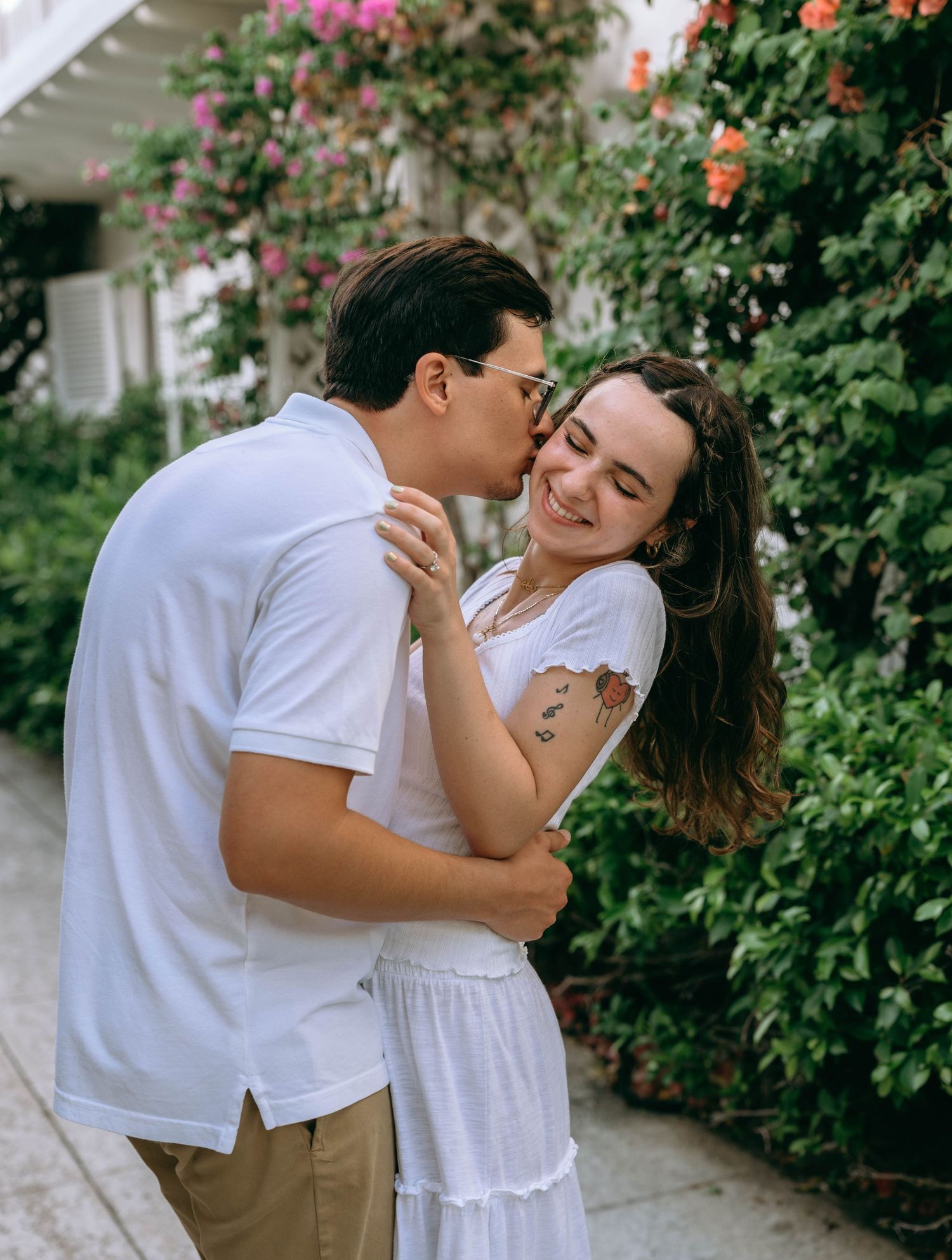 A couple embracing and sharing a kiss outdoors surrounded by colorful flowers. Engagement photos on Worth Avenue in Palm Beach, Florida.
