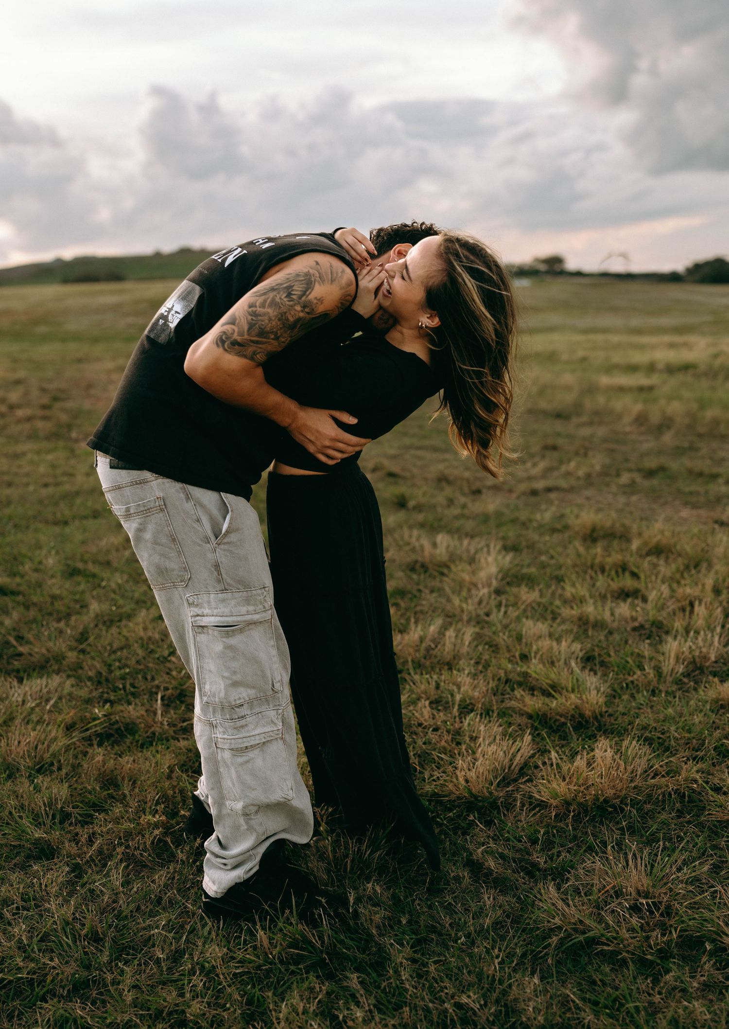 Two people performing a romantic dance dip in a grassy field at sunset.