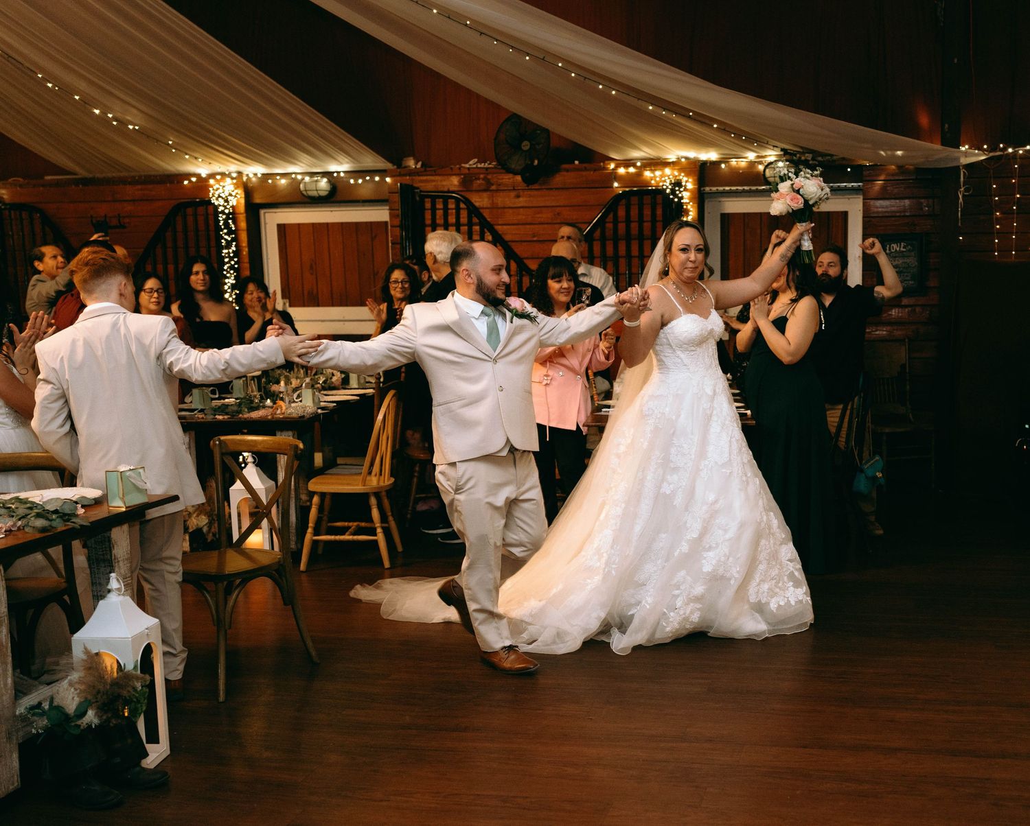 A group of wedding guests dancing together on a wooden dance floor during an evening reception celebration.