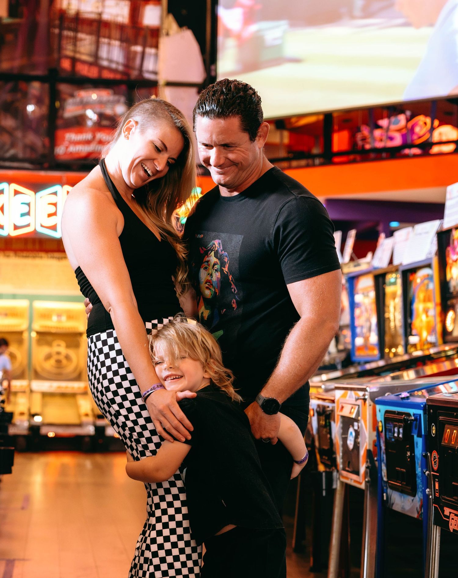 A happy family with a young child laughing together near arcade machines in a colorful game room.
