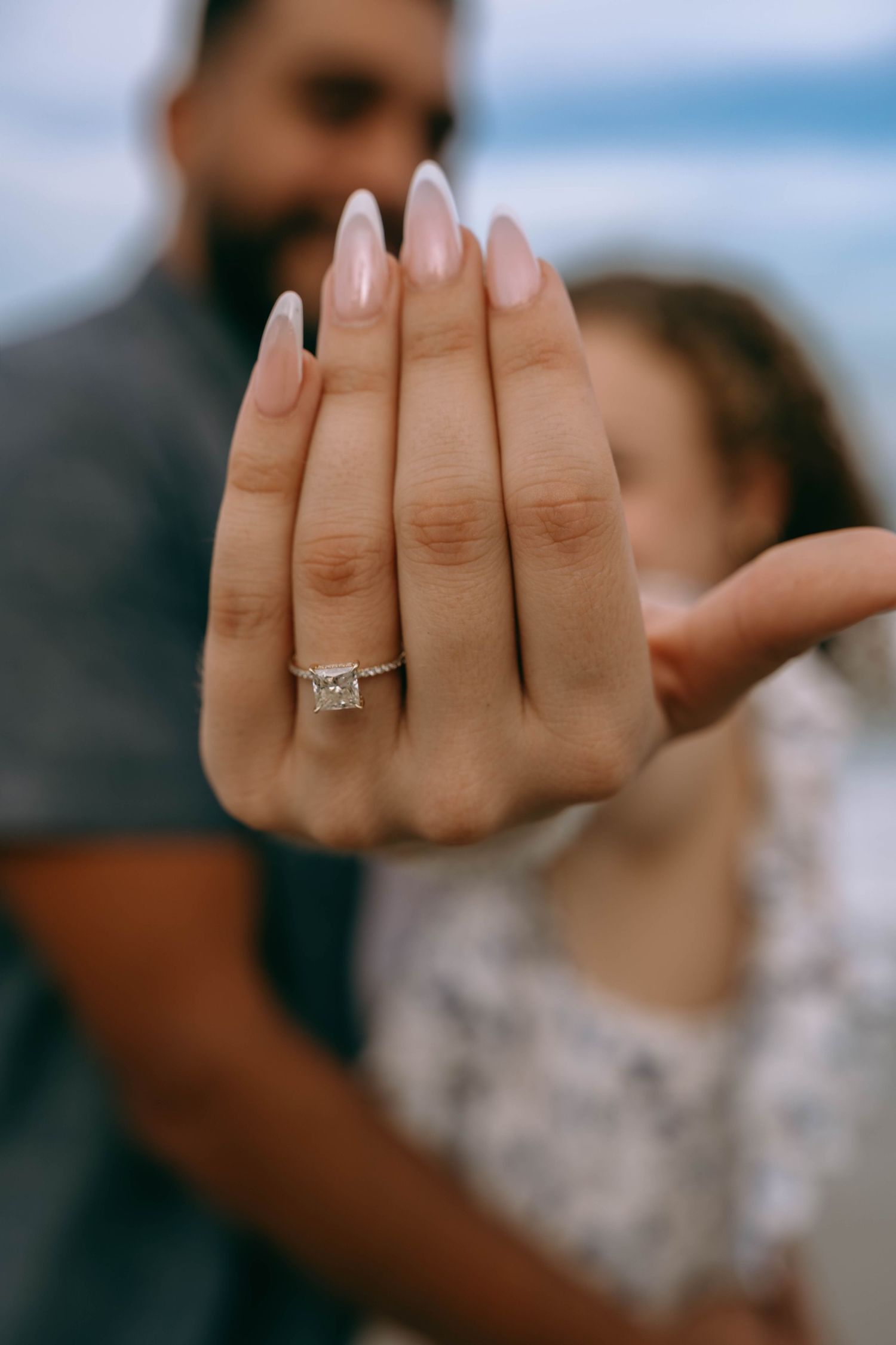 Close-up of a woman's hand displaying a stunning princess-cut diamond engagement ring on the beach on Worth Avenue Palm beach.
