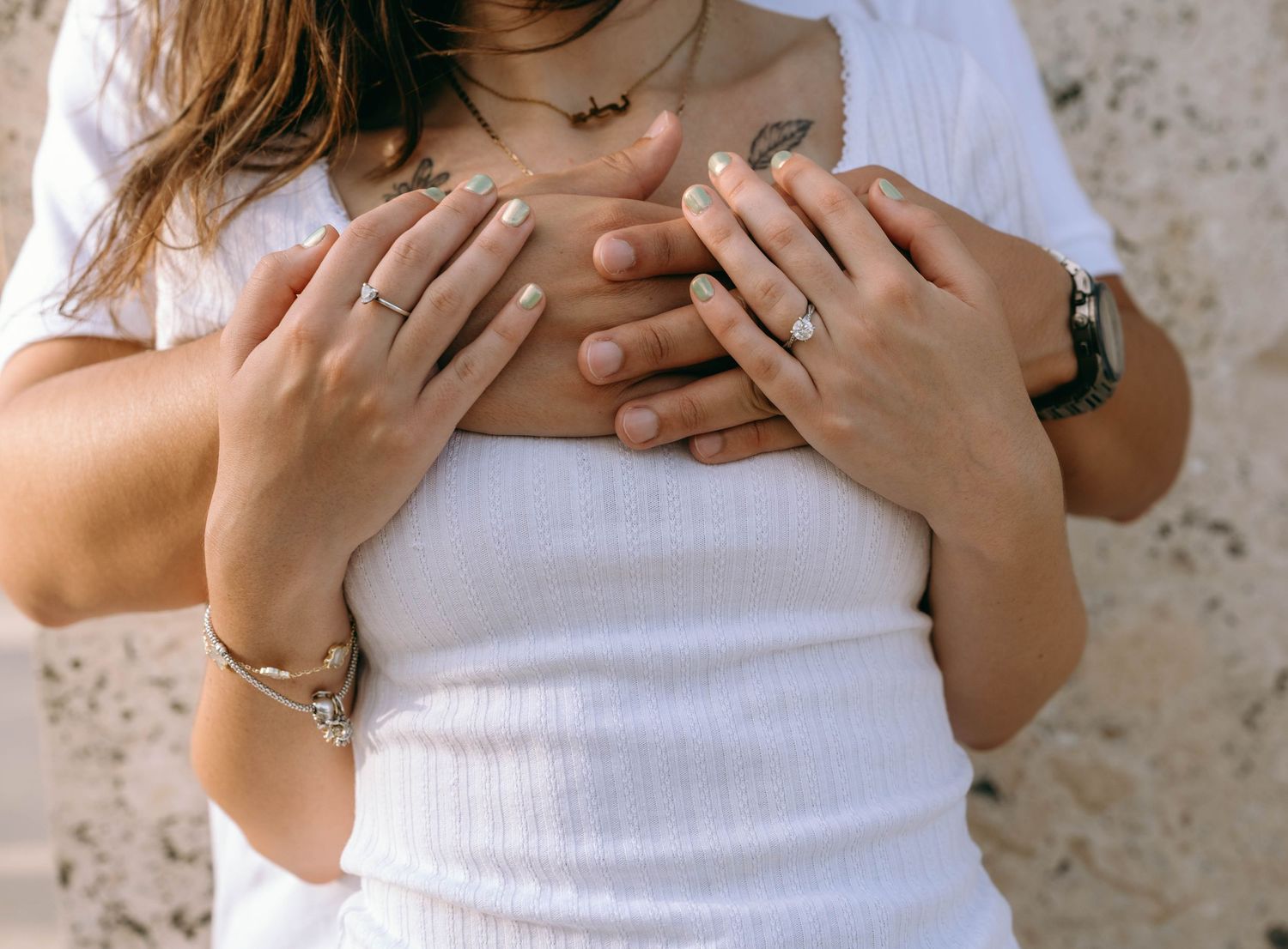 Couple embracing, woman in white top with rings and bracelet, hands placed on chest in romantic pose. Engagement photos on Worth Avenue