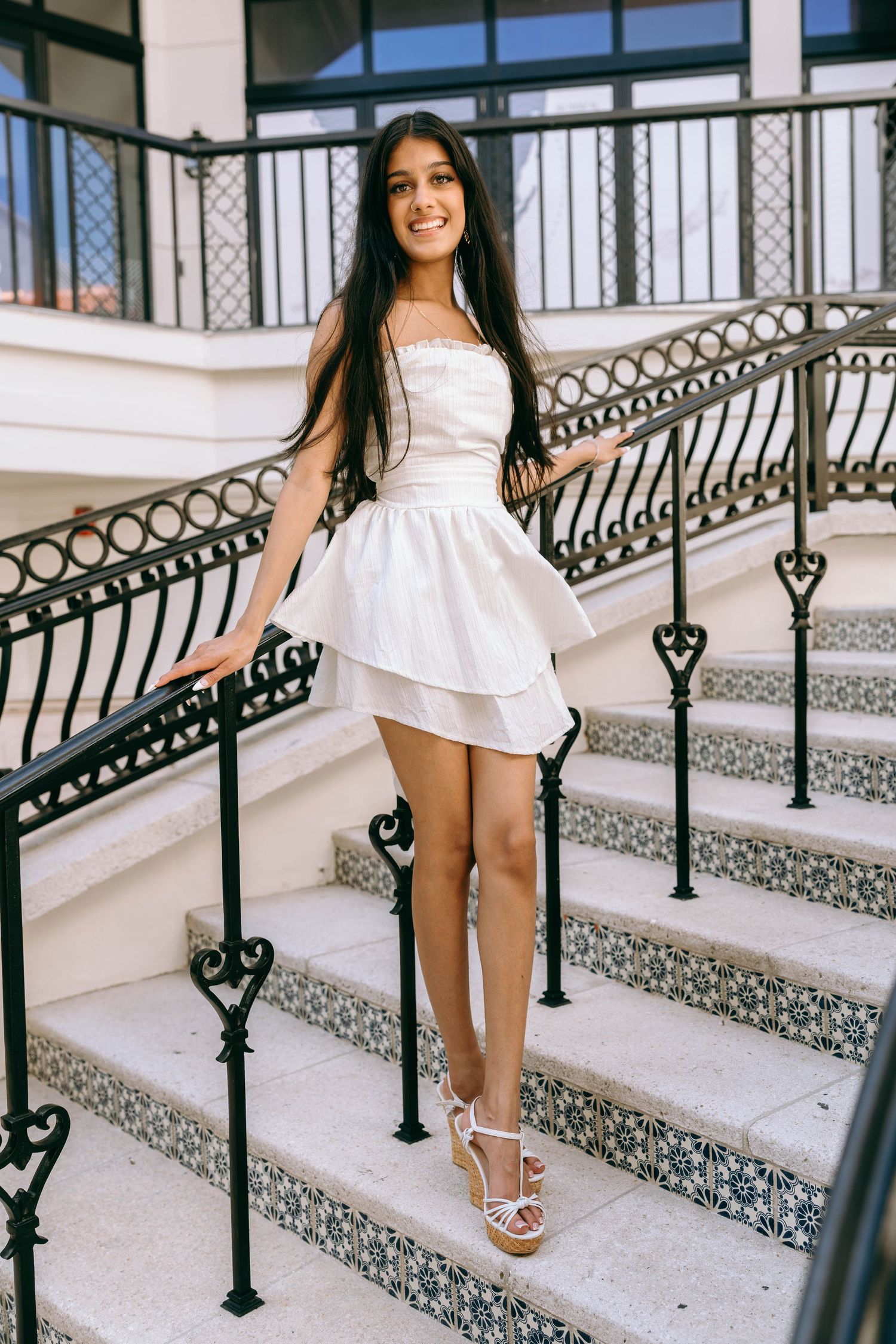 Smiling young woman in white layered mini dress posing on decorative tiled stairs on Worth Avenue Palm beach.