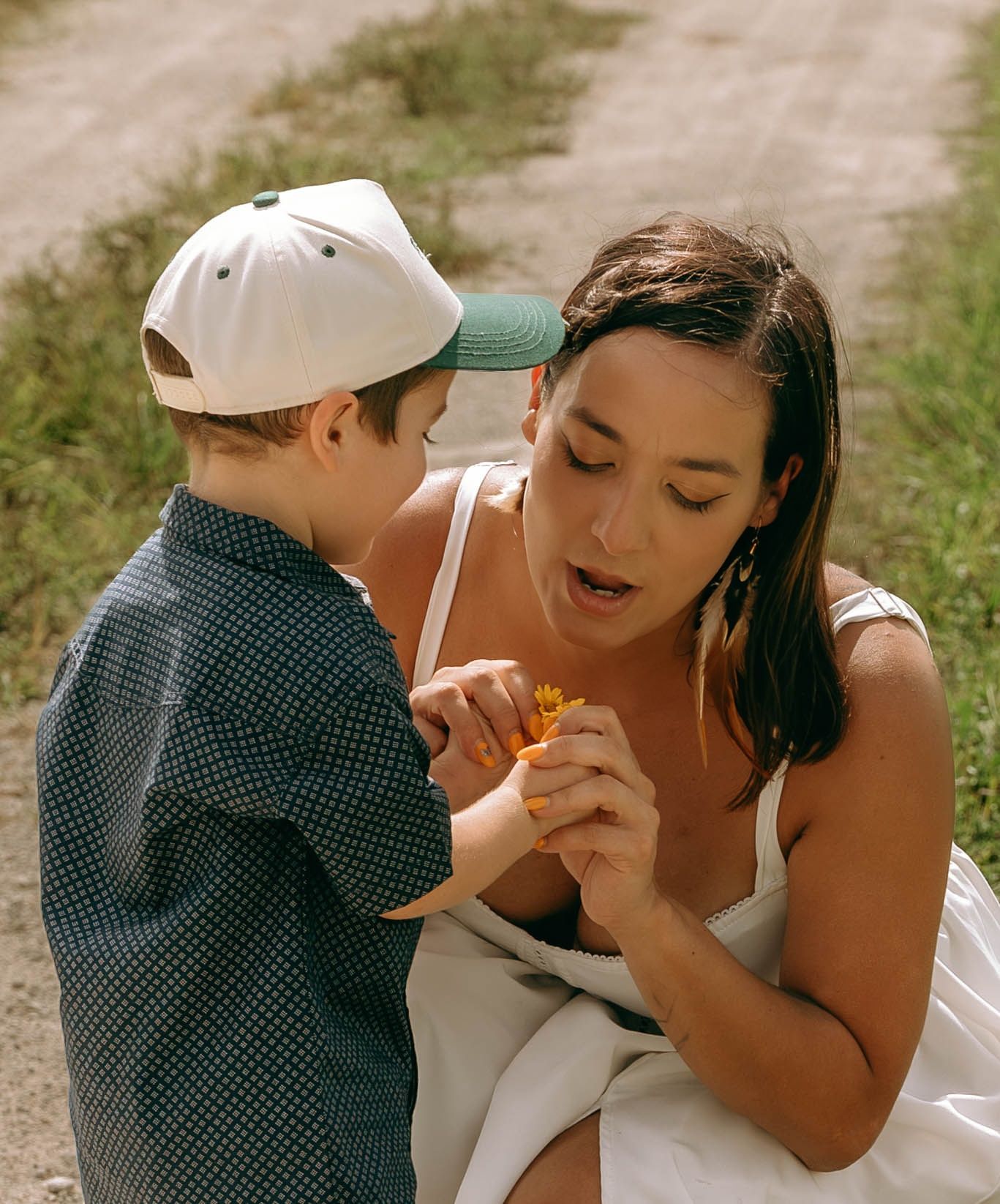 A woman and young boy in a baseball cap examine a small orange flower together outdoors.