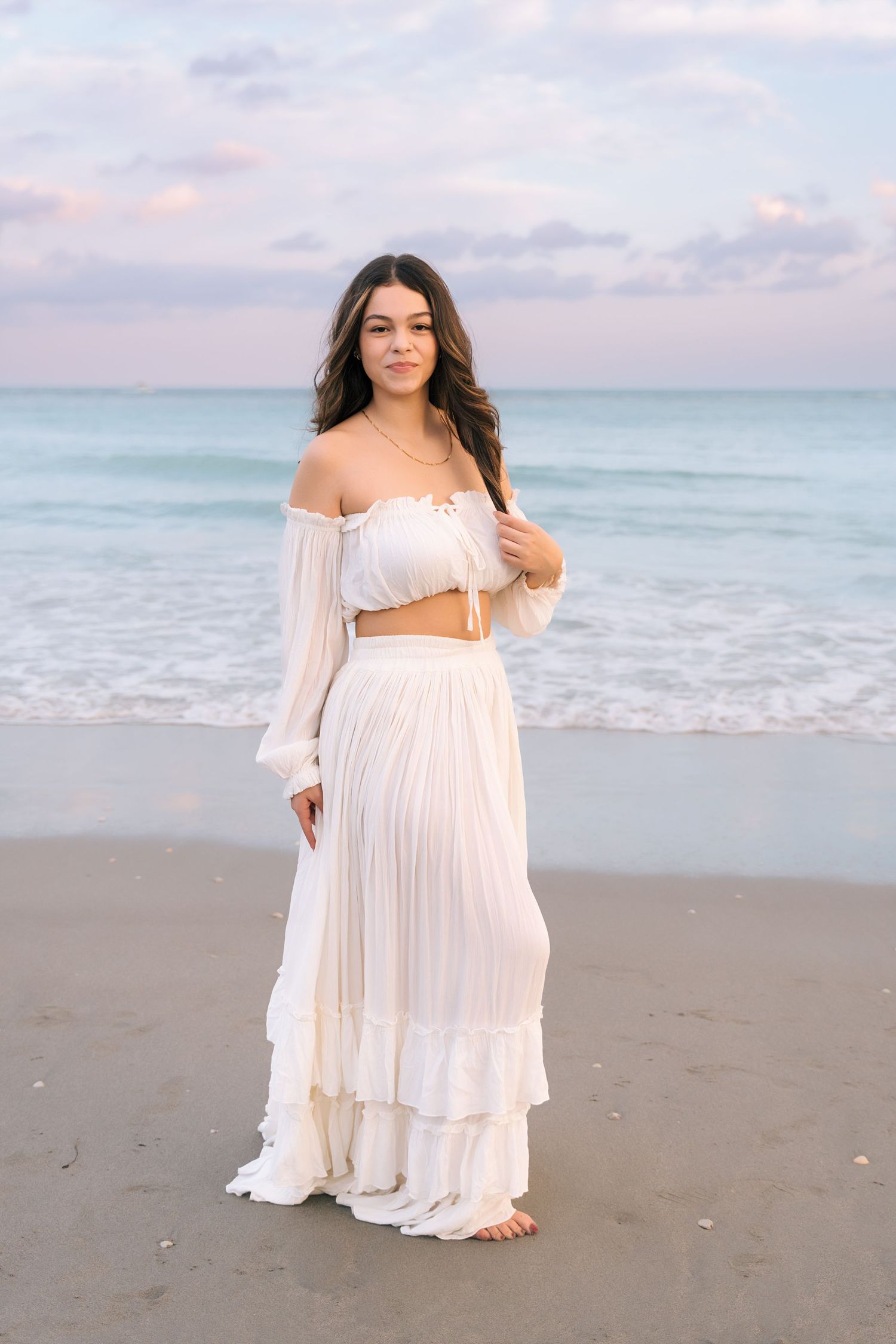 A flowy white maxi dress captured during a beach photoshoot at dusk.