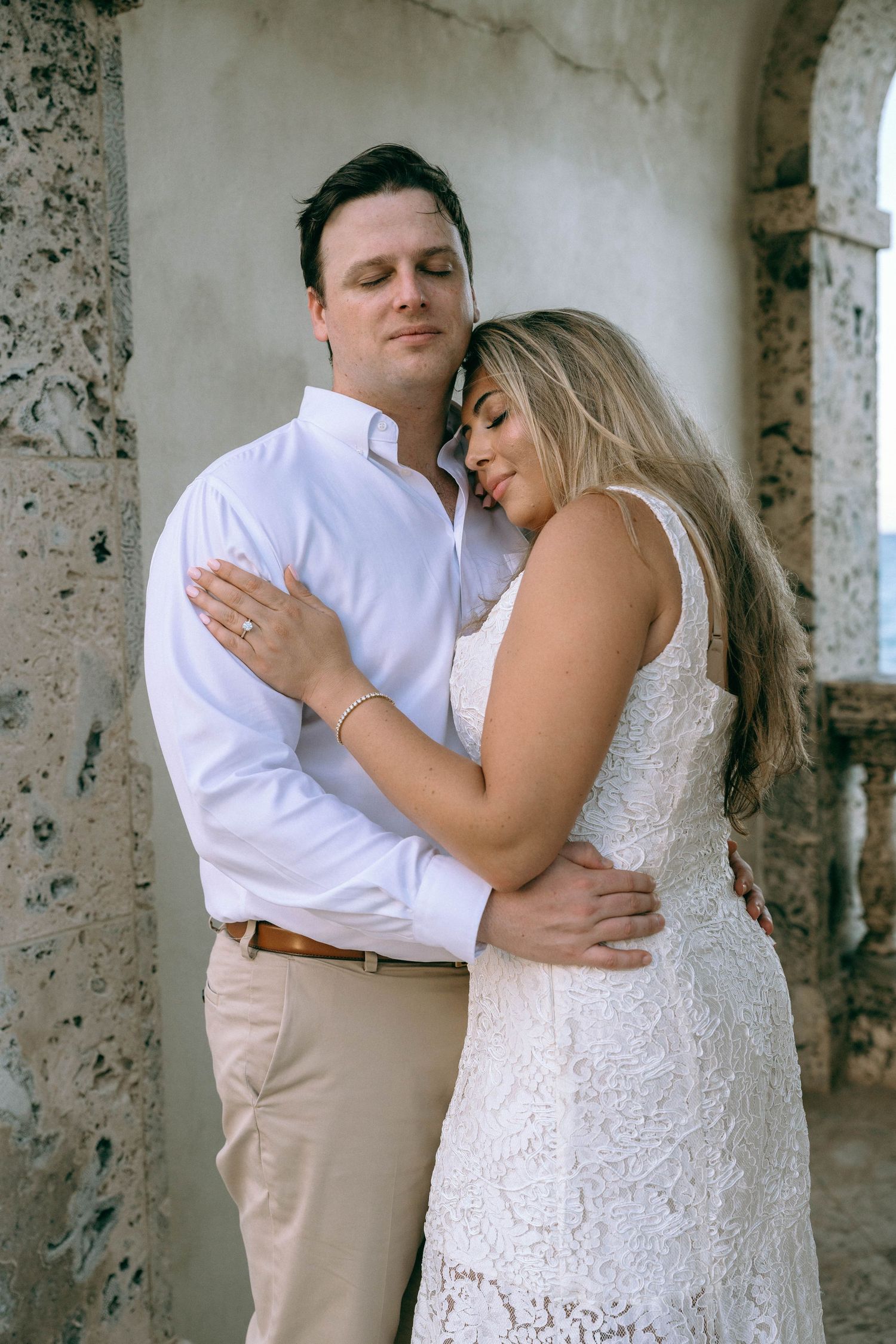 Couple sharing a tender embrace against a rustic stone wall in soft natural light.