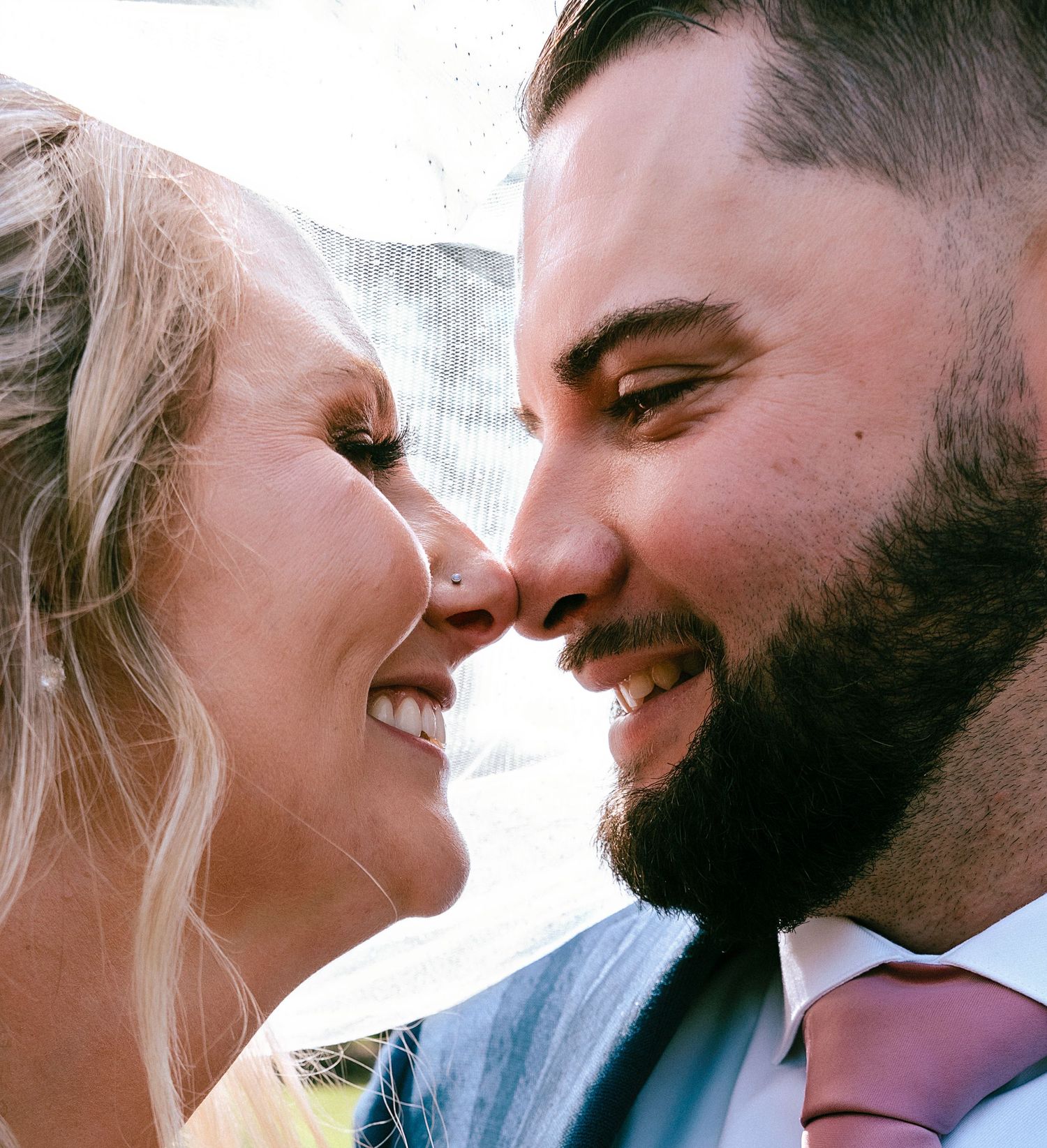 Close-up of smiling bride and bearded groom gazing at each other on their wedding day.