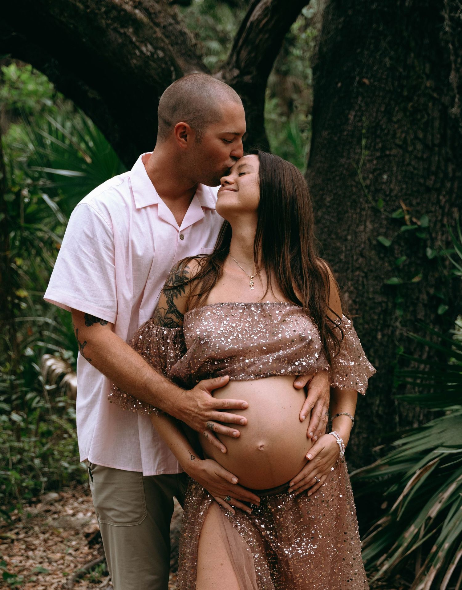 Maternity photos in forest setting with couple wearing coordinated neutral outfits.