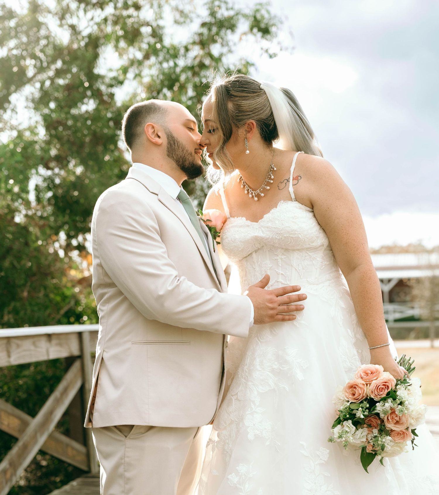 Bride in flowing white dress and groom in light suit embrace during outdoor wedding photo session.