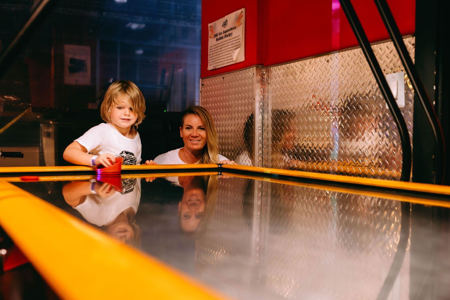 A woman and young child playing air hockey together at an arcade game center.