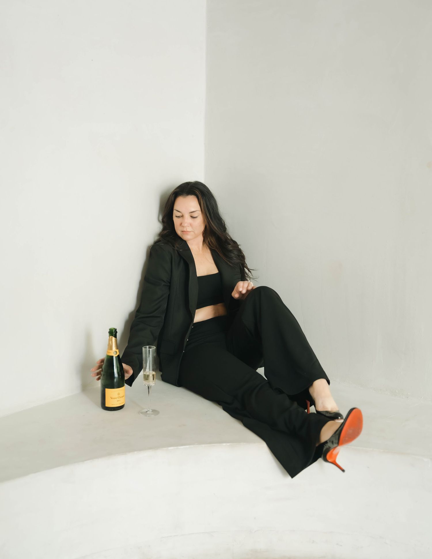 Person relaxing on floor wearing black outfit with champagne bottle nearby.