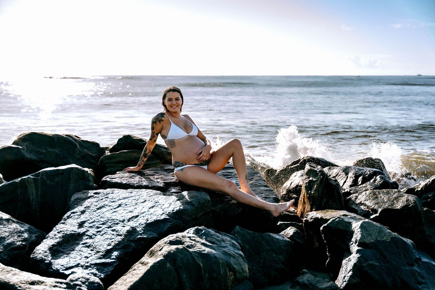 Artistic maternity photos captured on dark volcanic rocks by the ocean.