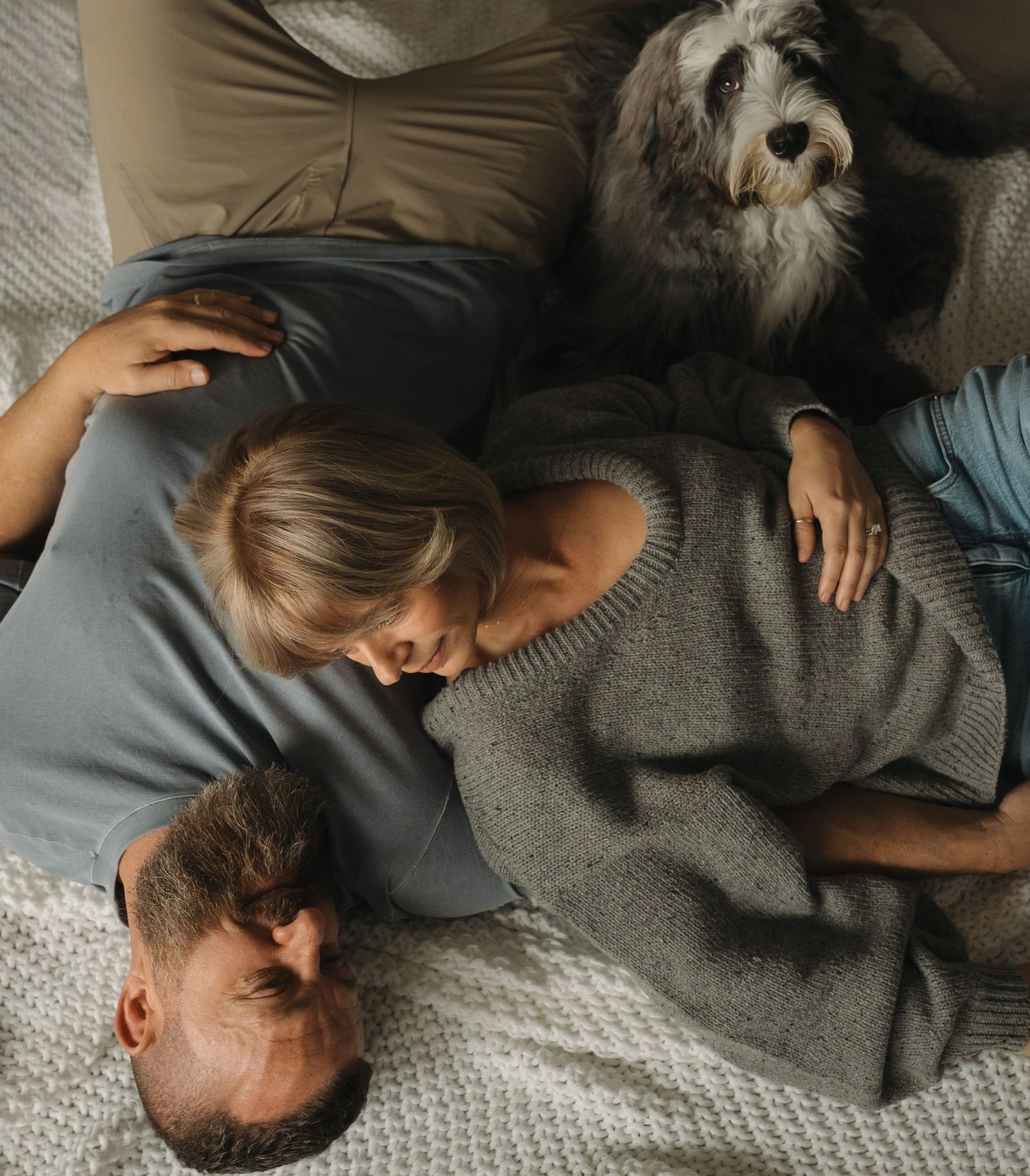 Overhead view of a fluffy grey dog resting on a textured blanket with others.