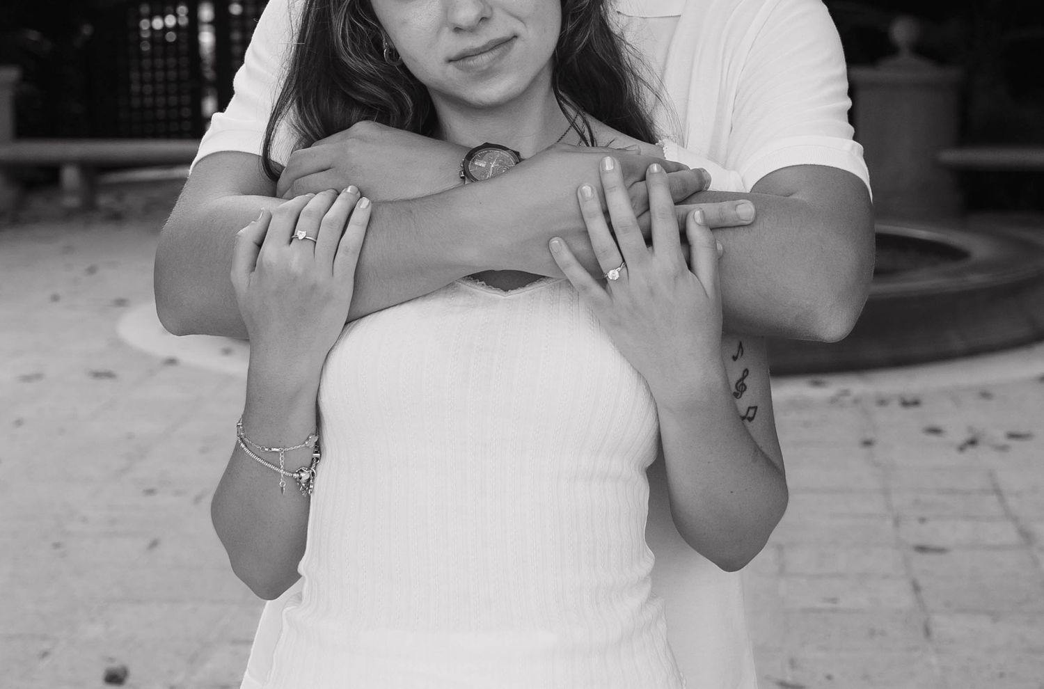 Black and white photo of a couple embracing, man wrapping arms around woman in white tube top outdoors. Engagement photos on Worth Avenue