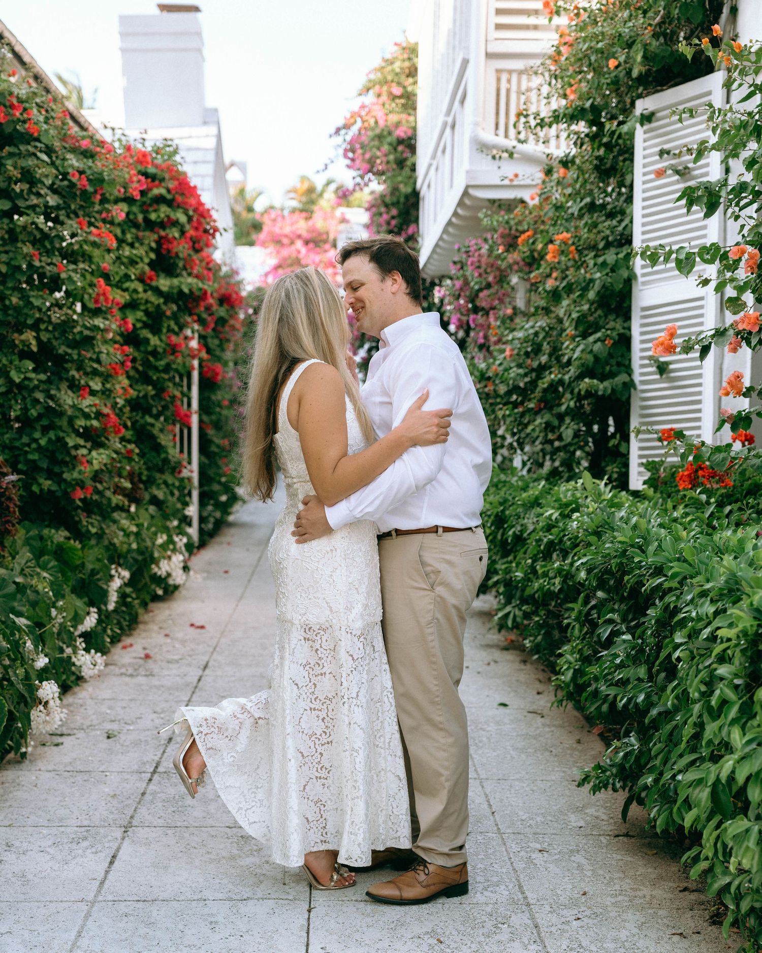 Couple sharing a romantic moment in a flower-lined garden pathway at sunset.