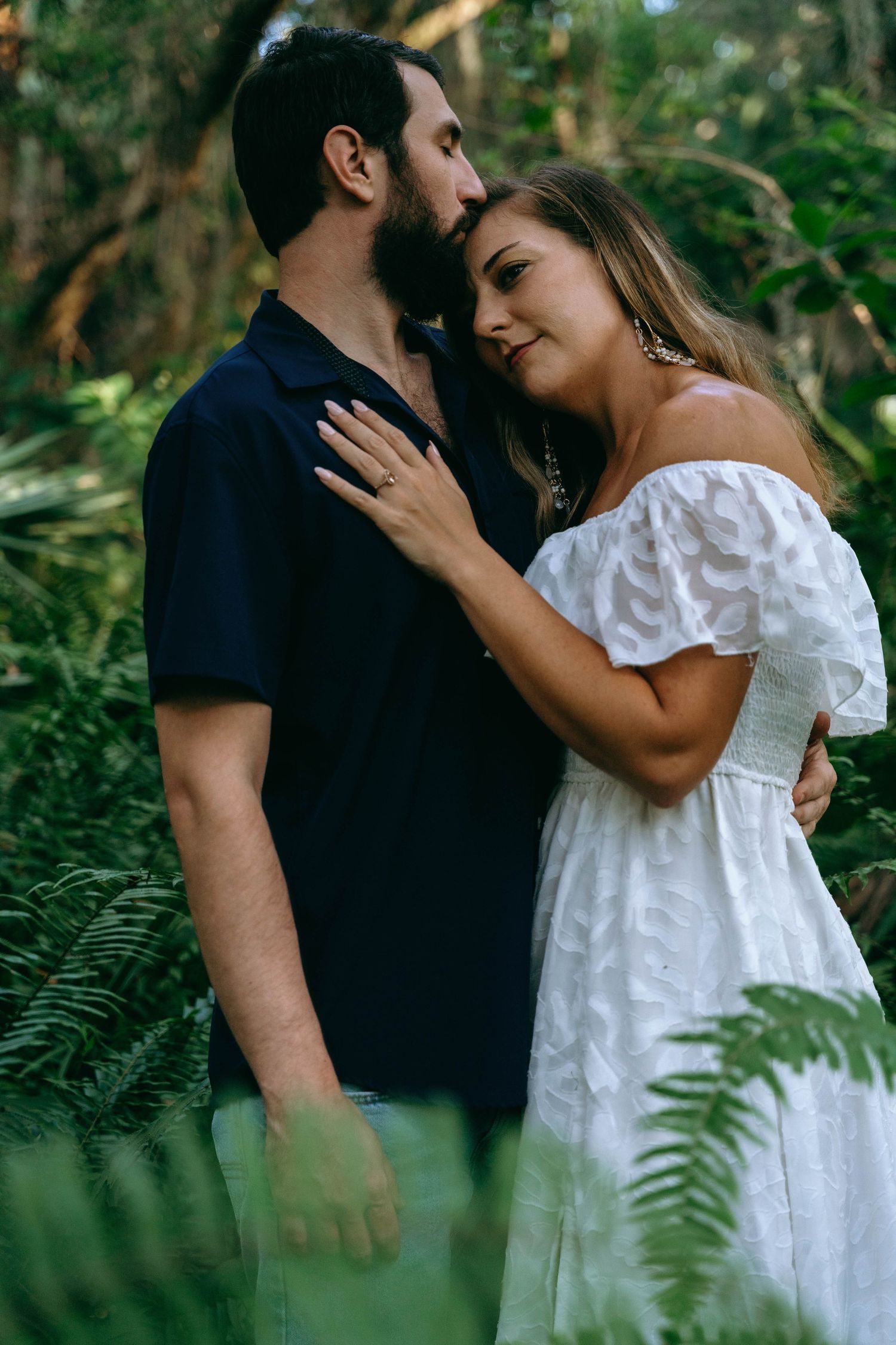 Romantic couple pose in tropical garden setting with white dress and navy shirt.