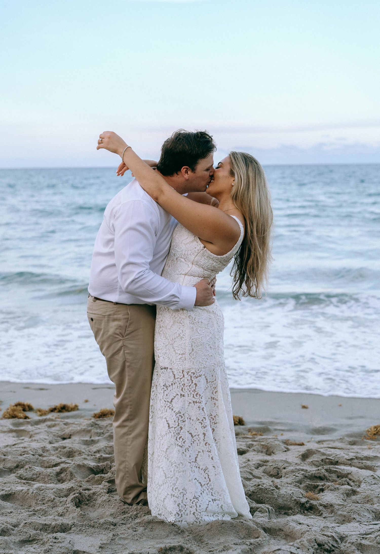 Couple sharing a passionate beach kiss at dusk with ocean waves in the background. Palm Beach, FL