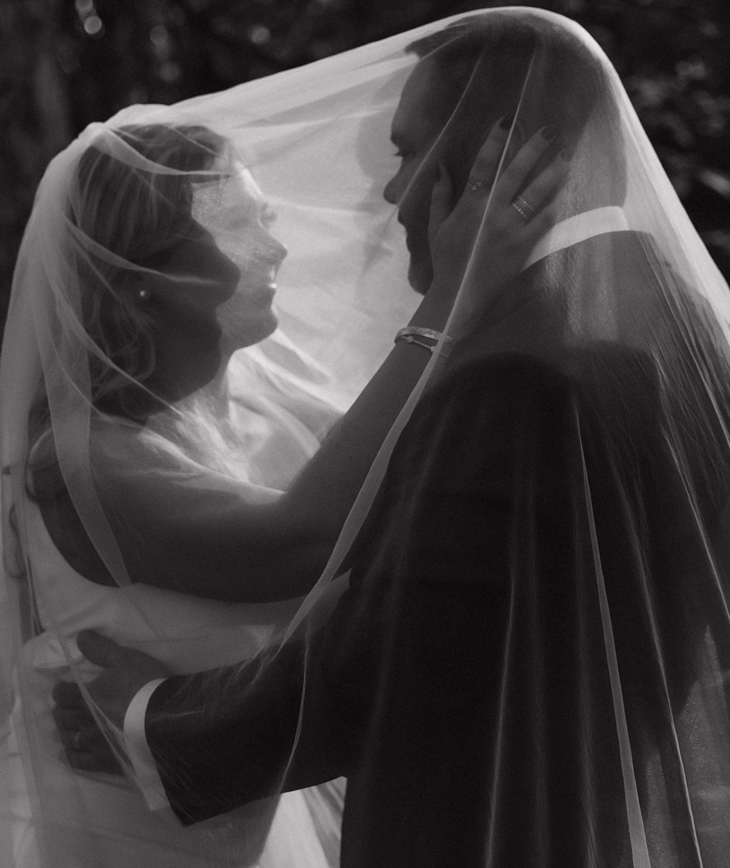 Black and white artistic silhouettes of couple embracing through flowing veil.