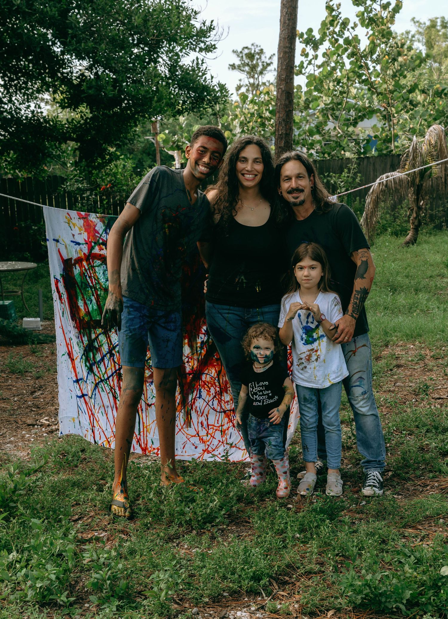 Family posing proudly in front of colorful abstract painted artwork outdoors.