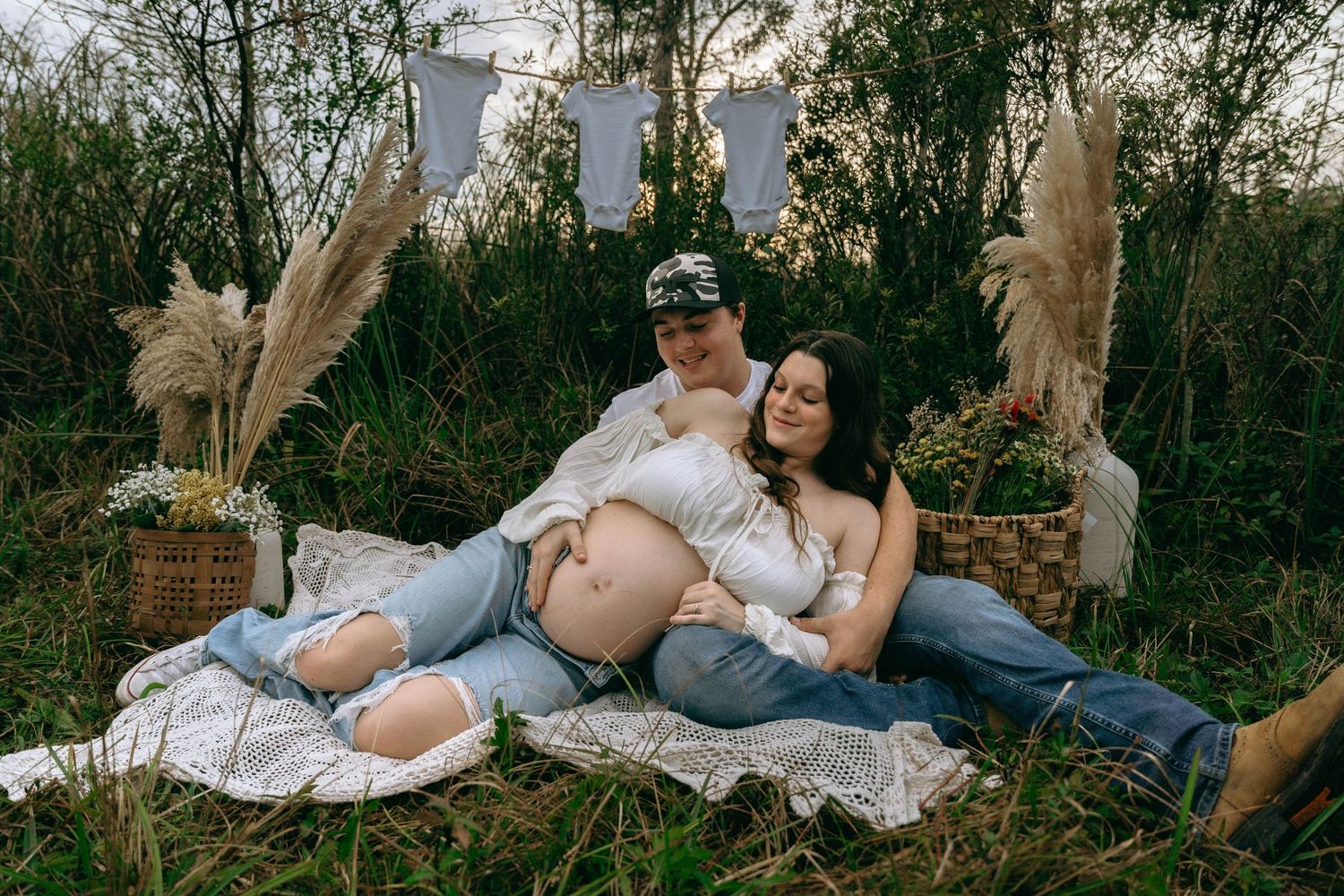 A romantic couple poses together on a blanket in a natural outdoor setting during a photo session.