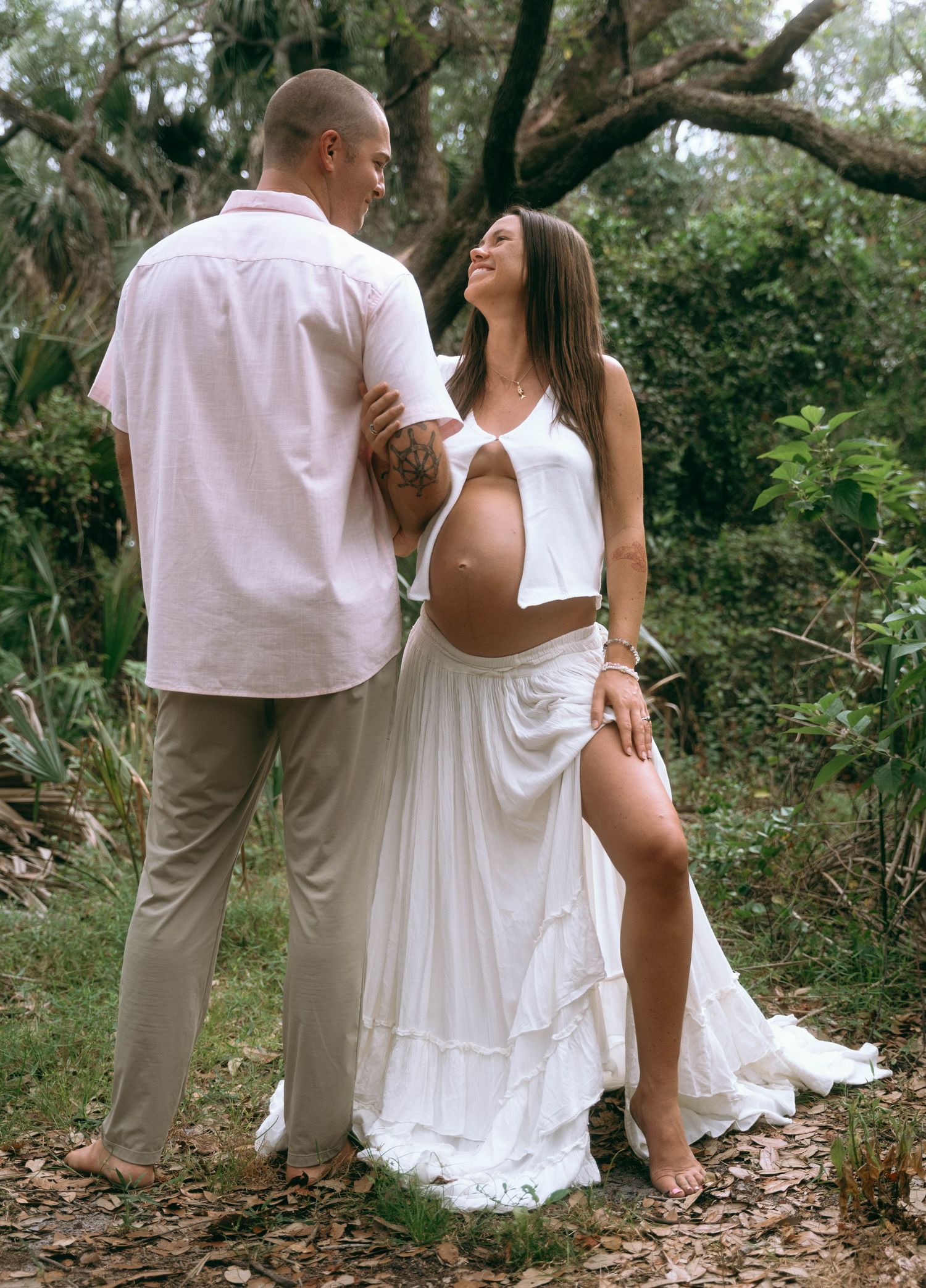Ethereal maternity photography session featuring flowing white dress in wooded setting.