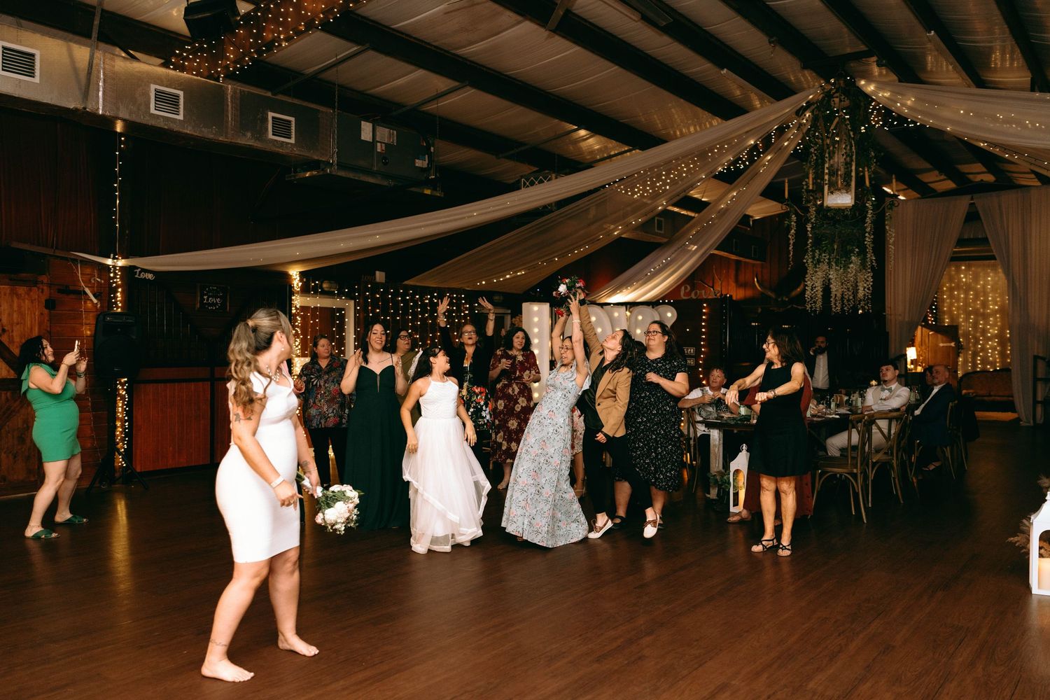 Wedding guests dance and celebrate on a rustic wooden dance floor under exposed beam ceilings.