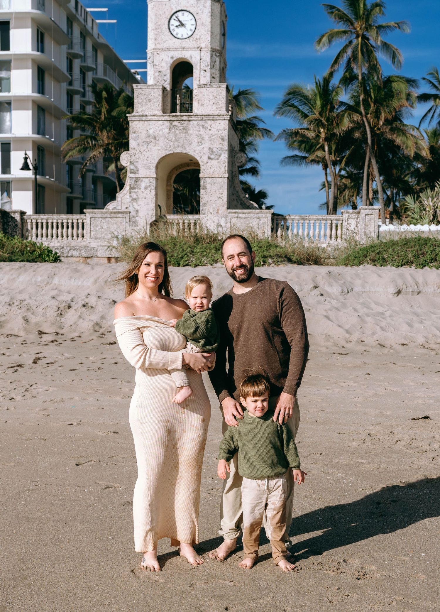 Family posing together on beach with palm trees and clock tower in background.