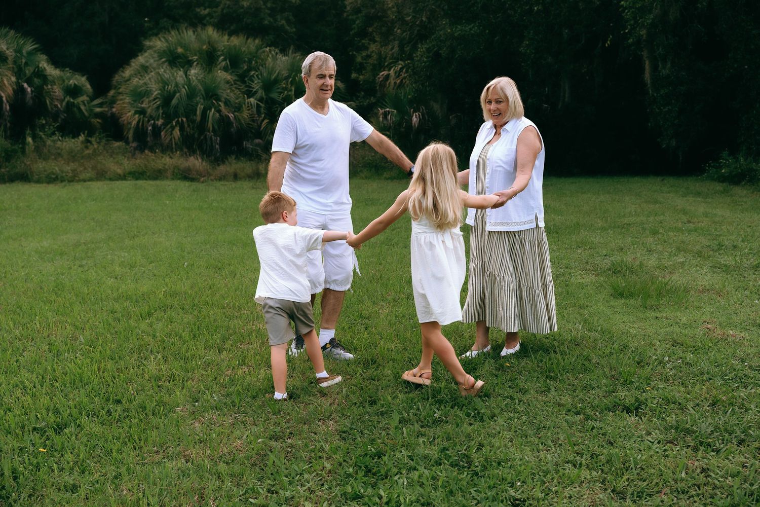 Grandparents and grandchildren play ring around the rosie on a sunny green lawn at Riverbend Park in Jupiter, FL.