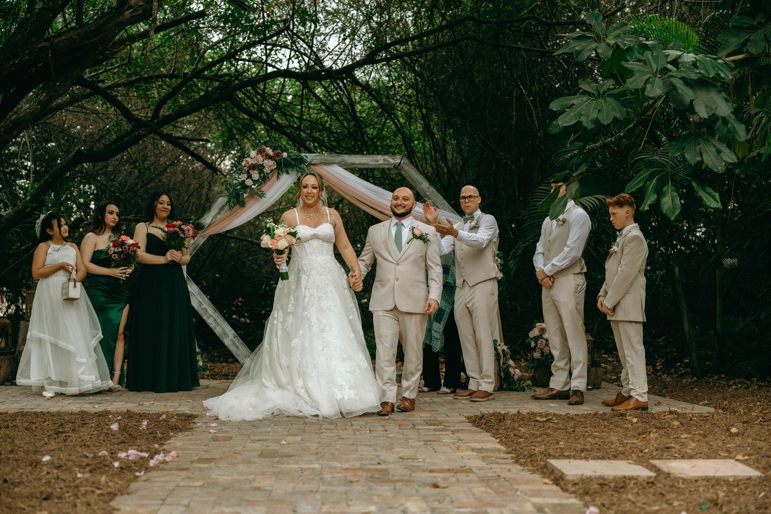 Wedding party poses together for joyful photos in a lush outdoor garden setting during summer celebration.