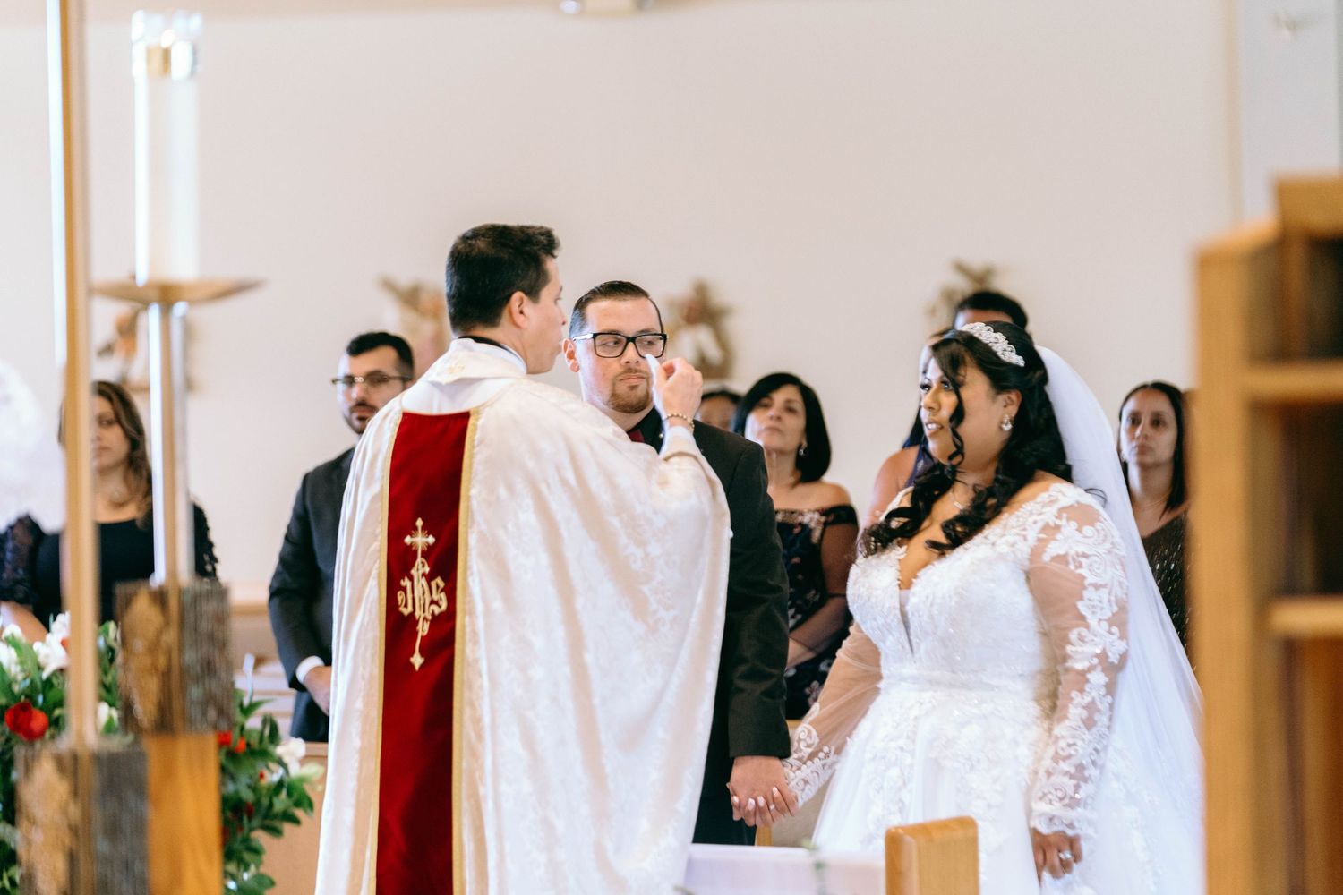 Indoor church wedding ceremony with decorative red accents and white floral arrangements.