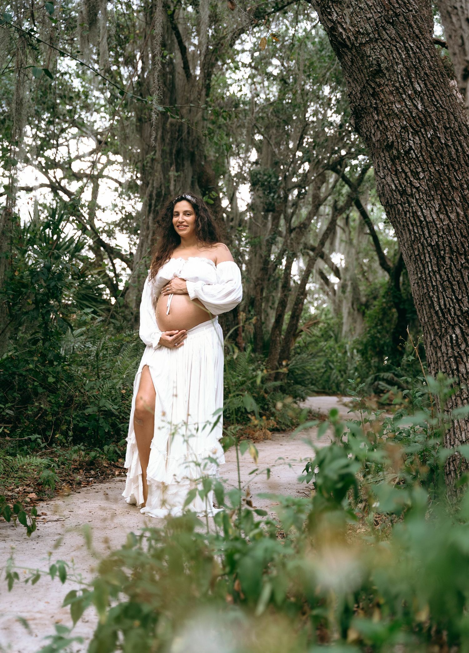 A flowing white dress creates an ethereal scene among Spanish moss-draped trees.