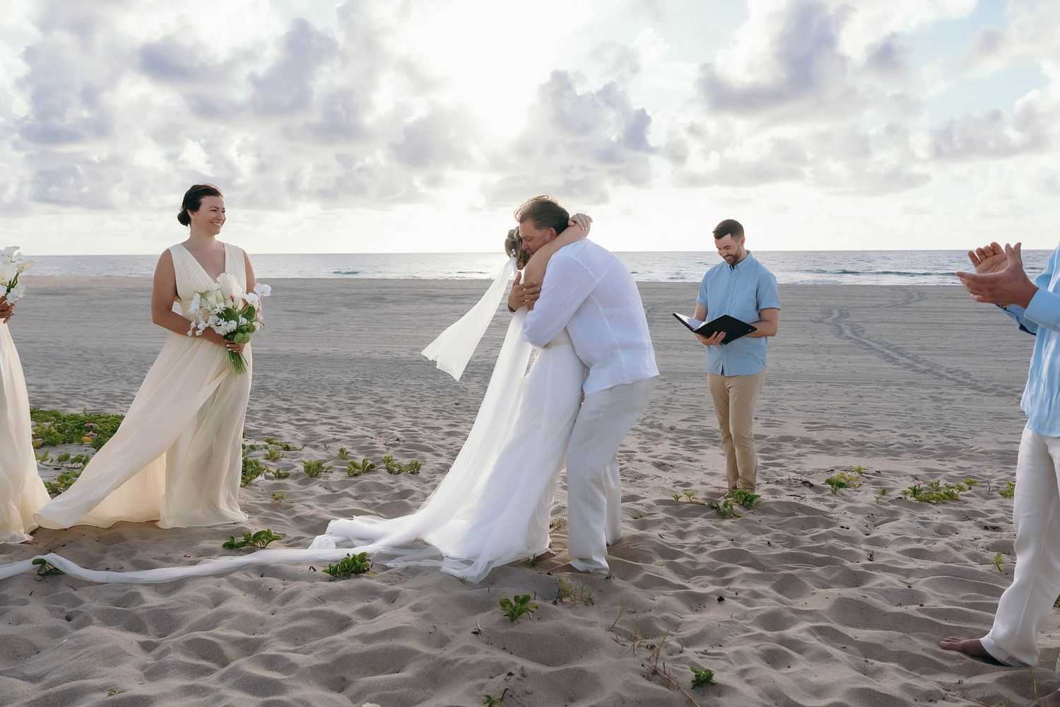 Wedding party walking along beach shore in white attire.