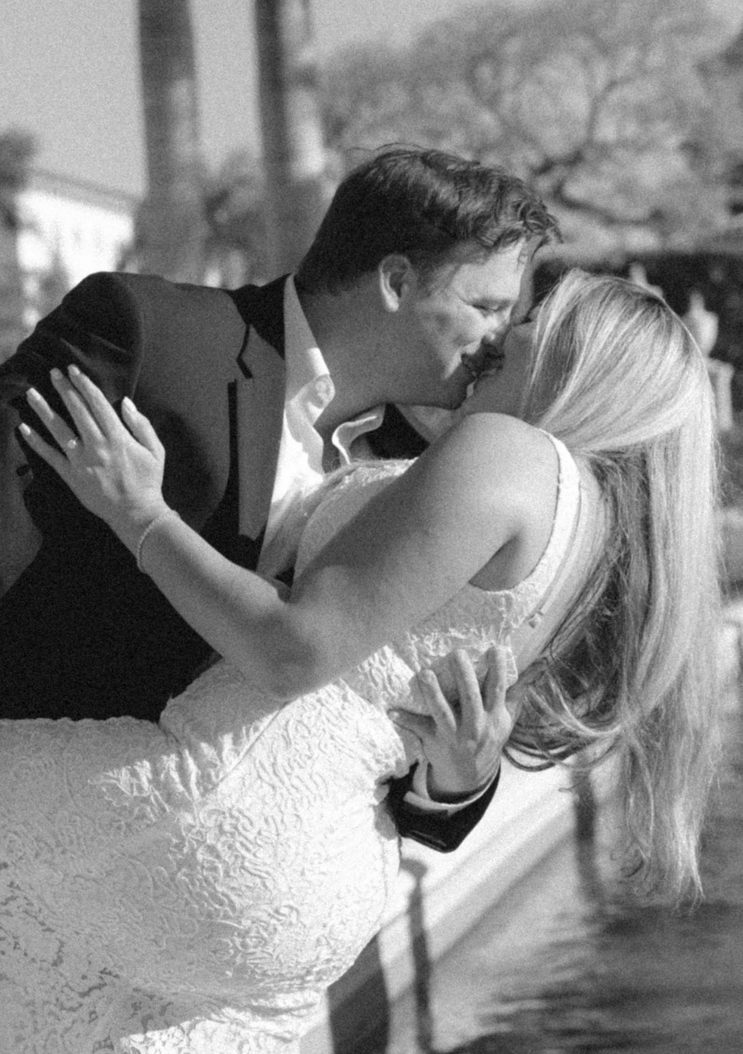Black and white photo of a bride and groom sharing a romantic kiss at their wedding ceremony.