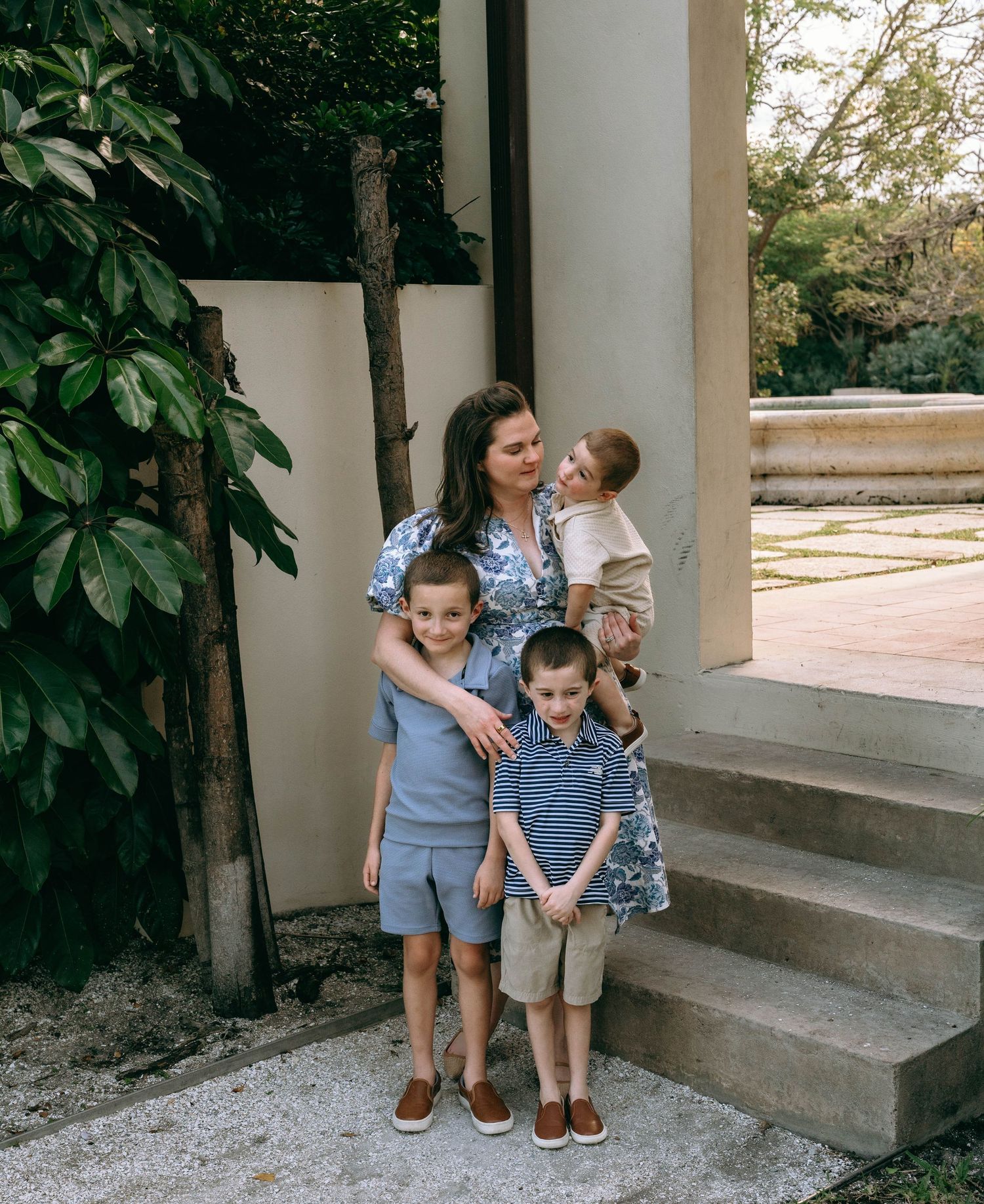 A woman poses with three young boys on garden steps near a white column and lush greenery.  Family photos at Bradley Park Palm Beach, FL