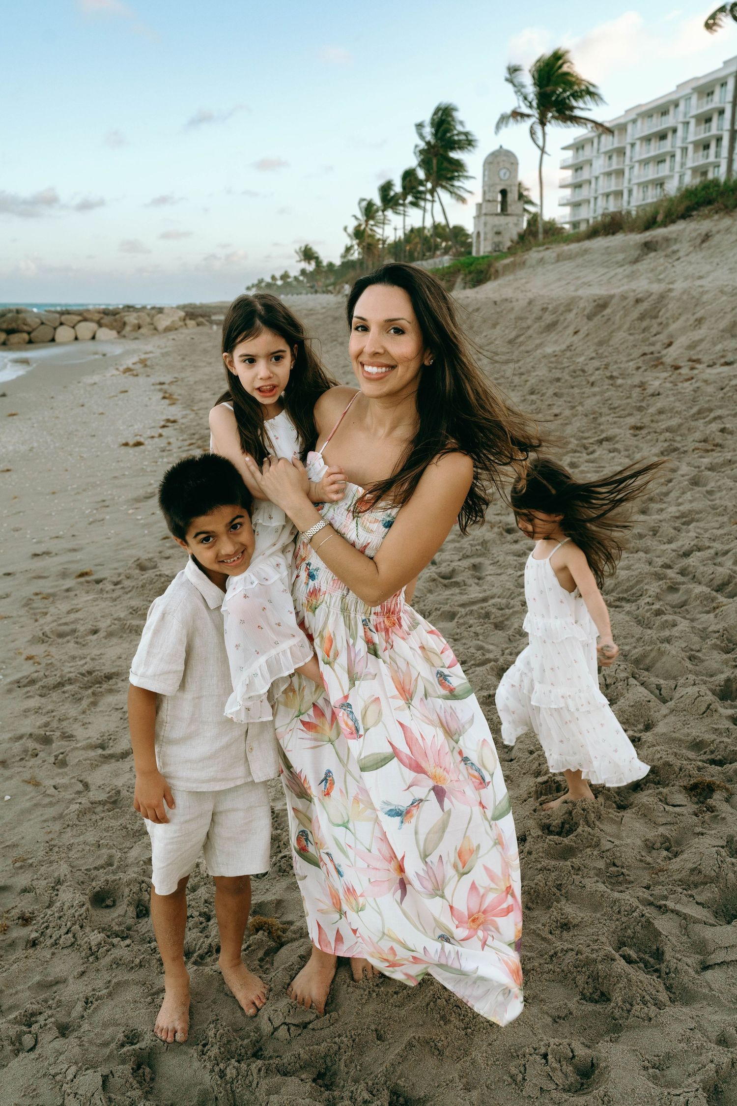 A smiling mother in a floral maxi dress poses with her three children on a sandy beach at dusk. Worth Avenue, Palm Beach, FL