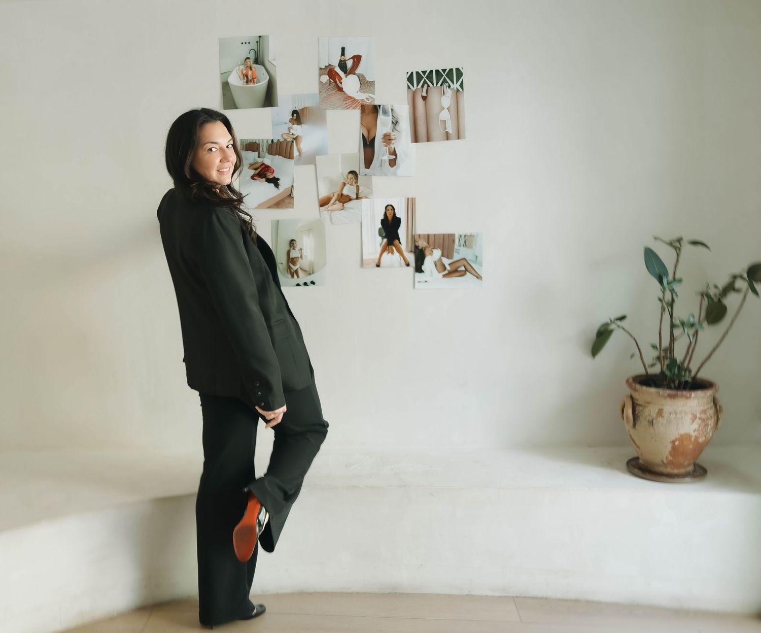A woman in black outfit stands against white wall with photo gallery display.