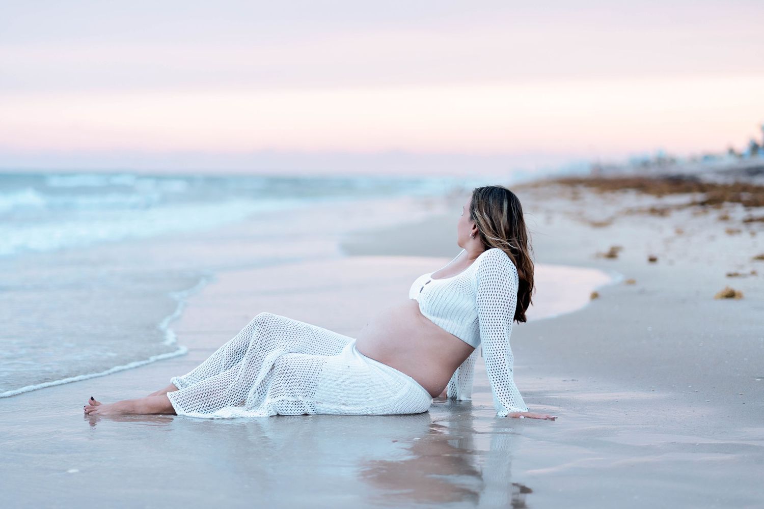 A peaceful beach scene with a figure resting by the water's edge at dusk.