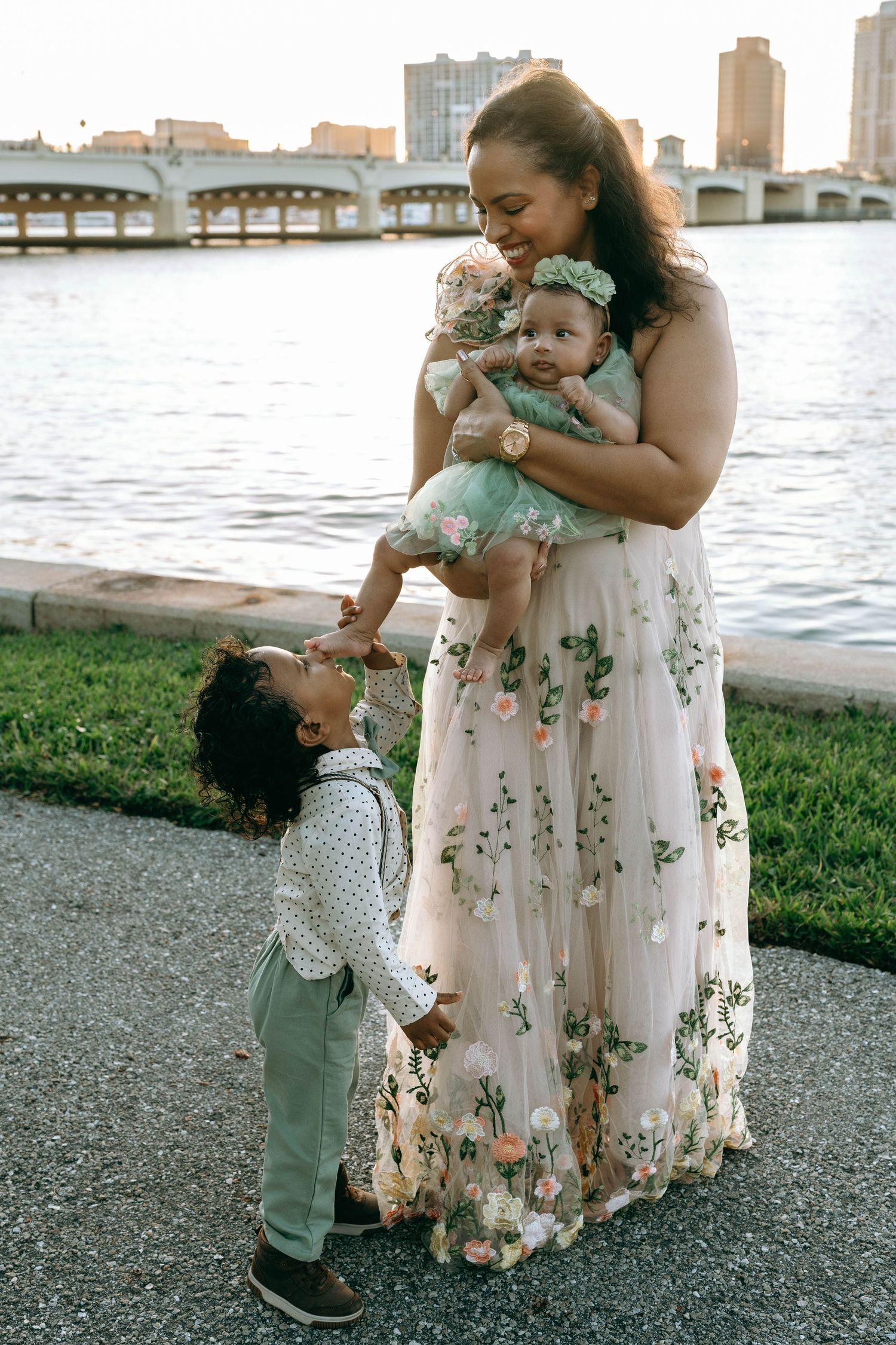 A tender moment captured in a series of photos showing a parent and child interacting by the waterfront in floral dress attire.