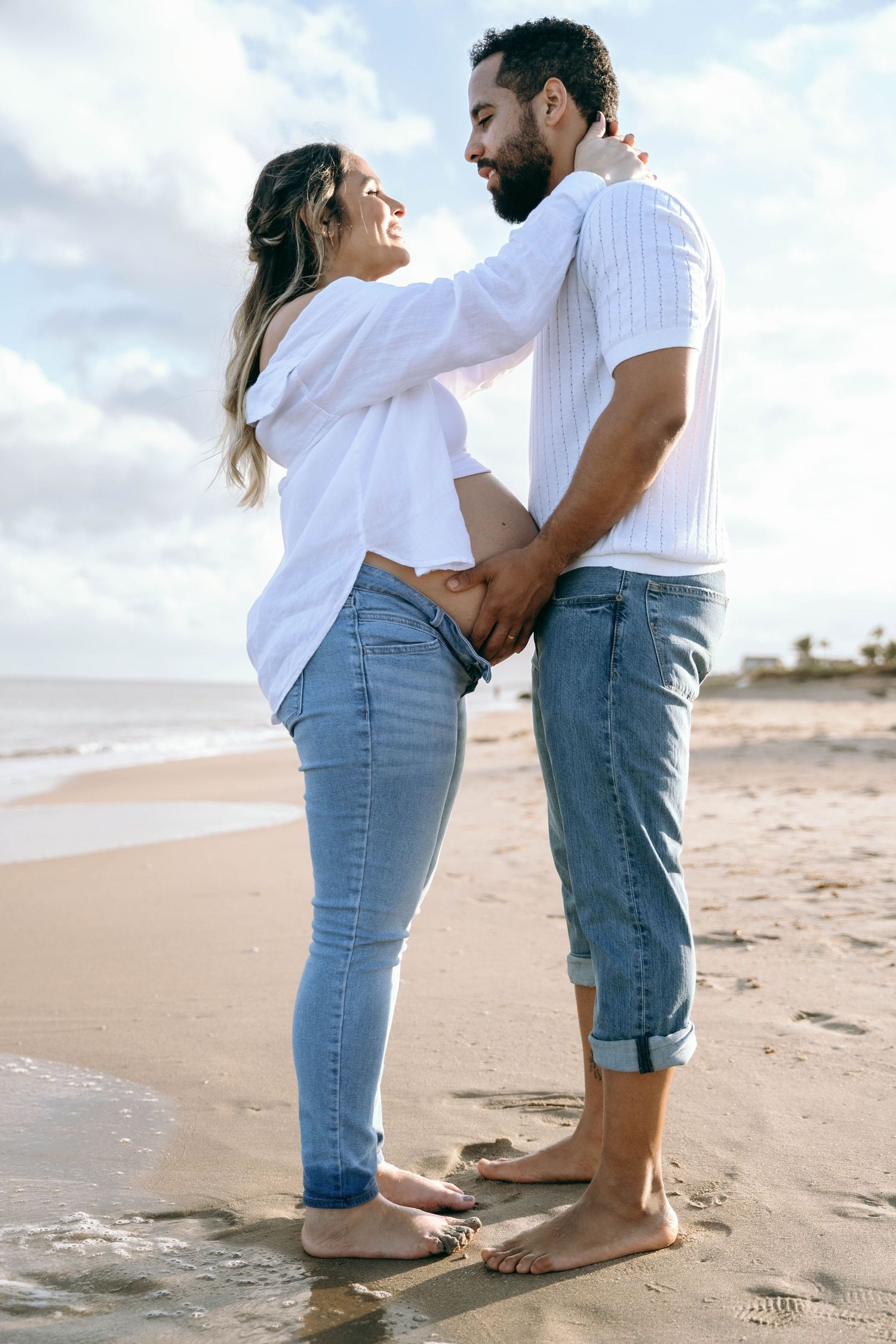 A romantic maternity photo of a couple embracing on the beach at sunset.