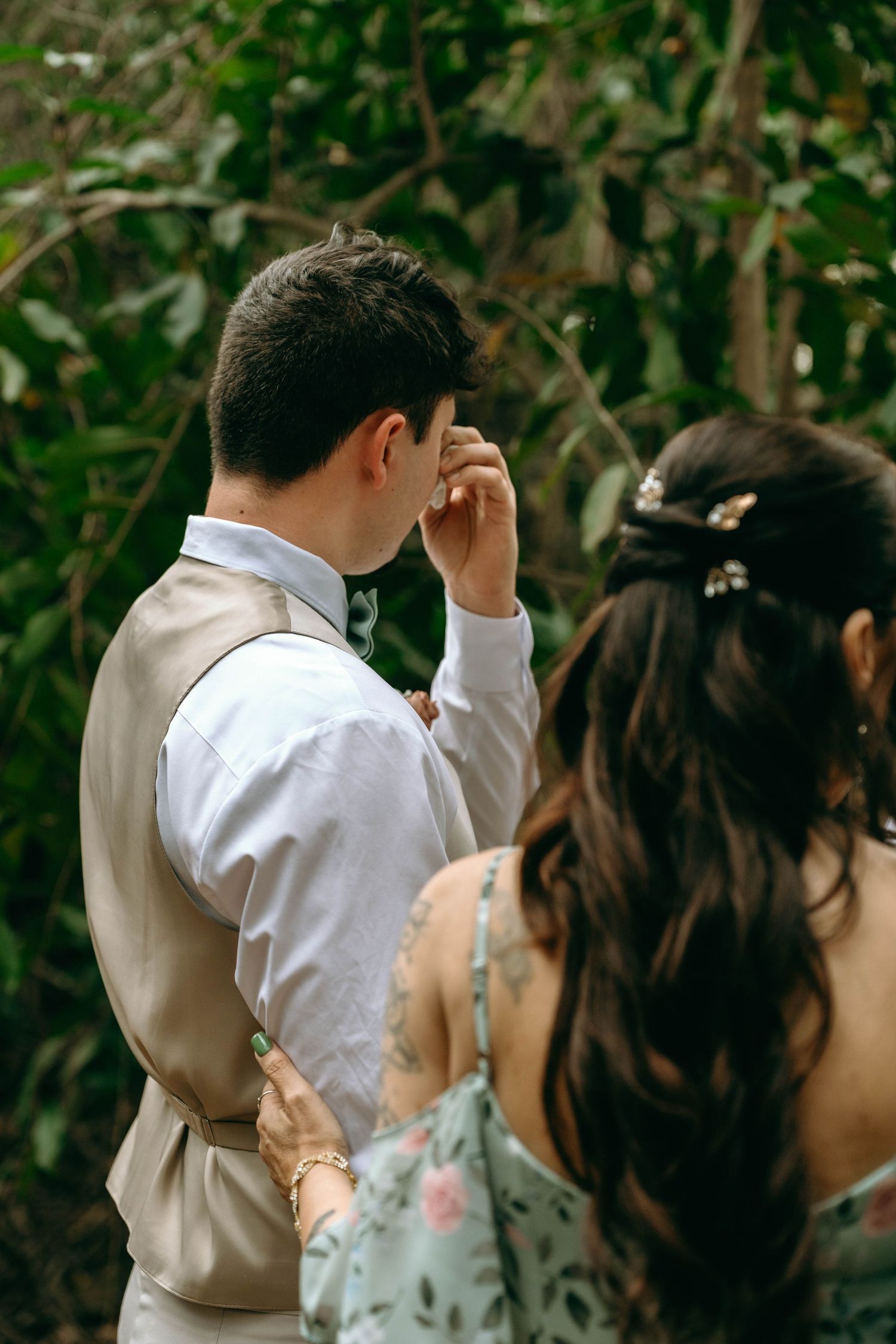 A couple at a wedding ceremony shares an emotional moment outdoors with greenery in the background.